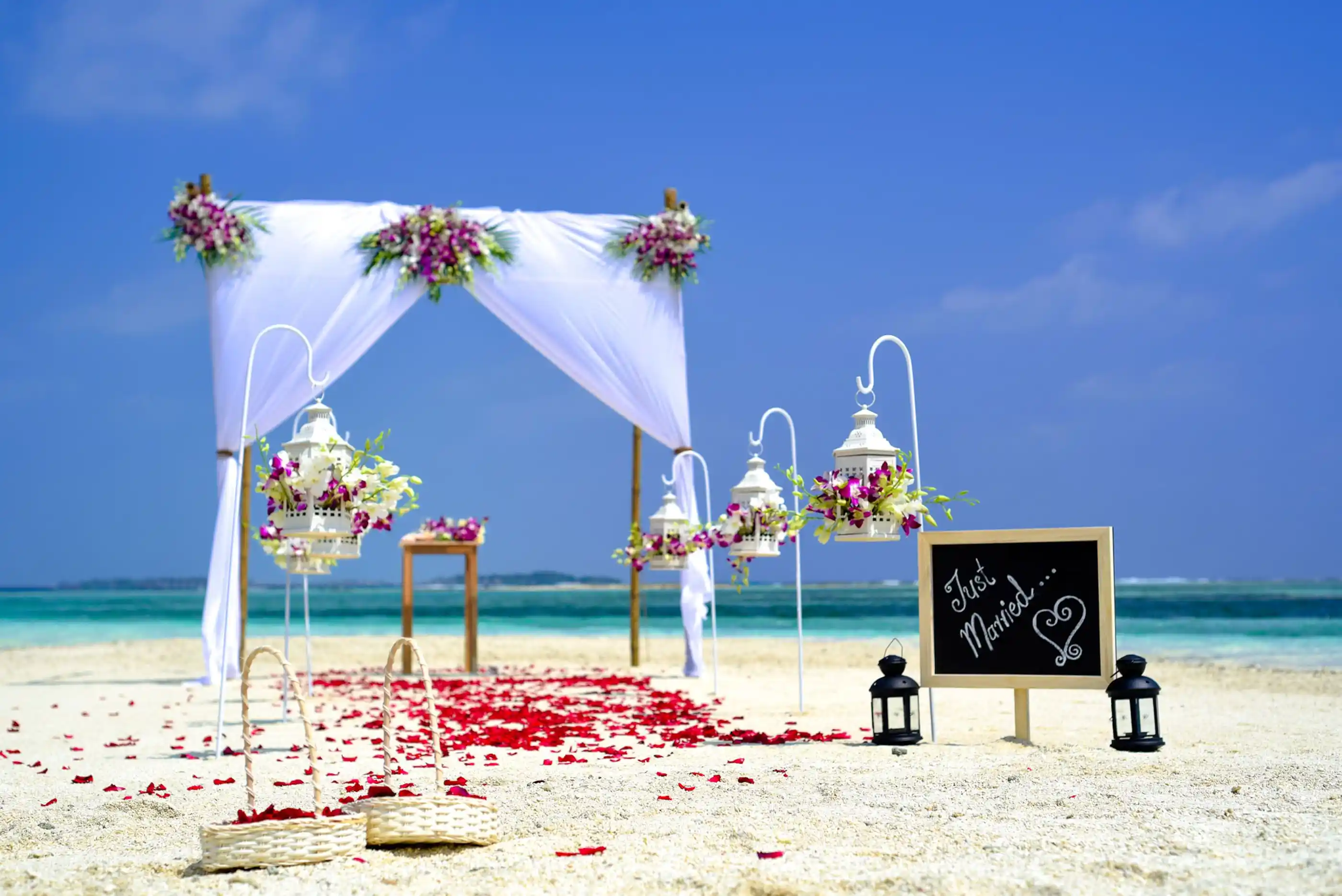 A beach ceremony set with flowers and lanterns at the water line