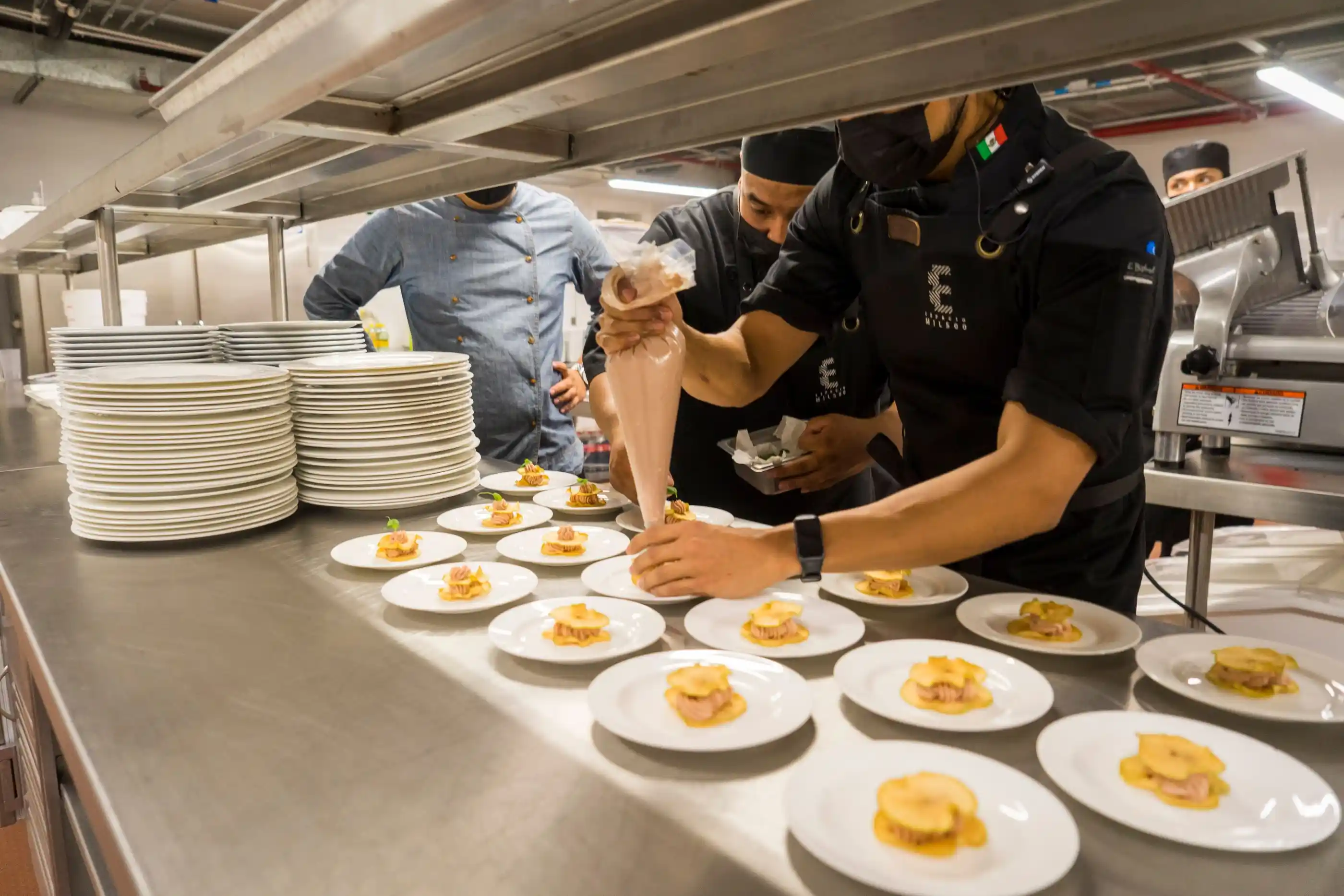 Chefs plating dishes along a pass in a working kitchen
