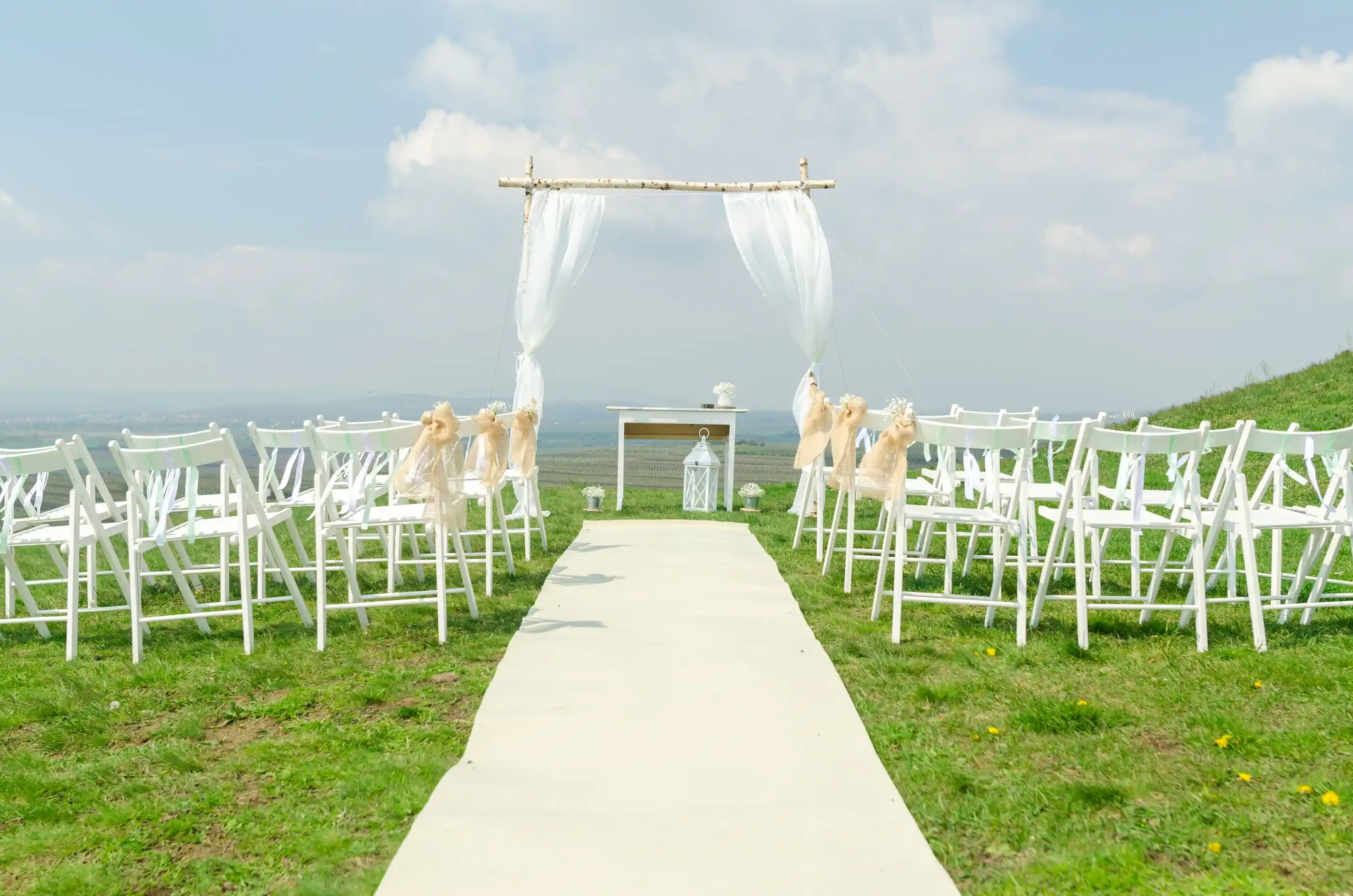 Rows of white chairs facing an arch on open grass under blue sky