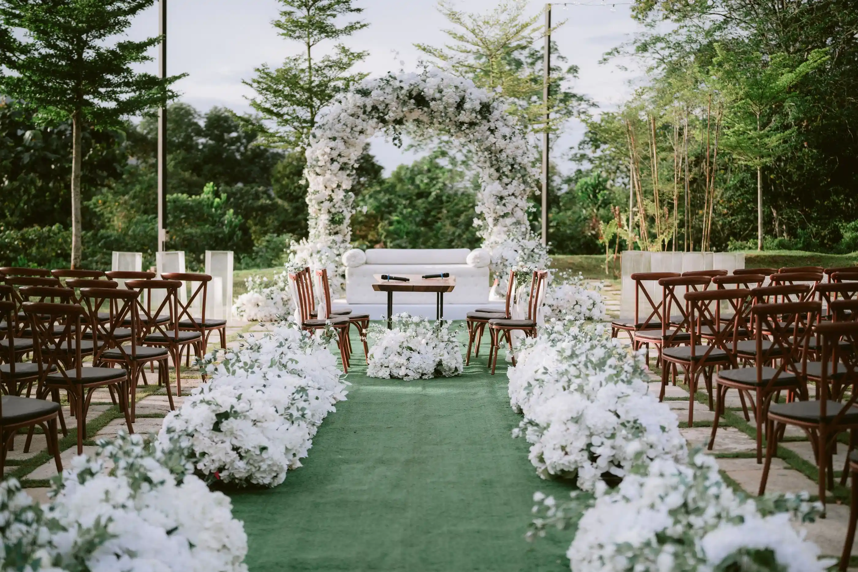 A white floral arch at the end of an aisle lined with blooms