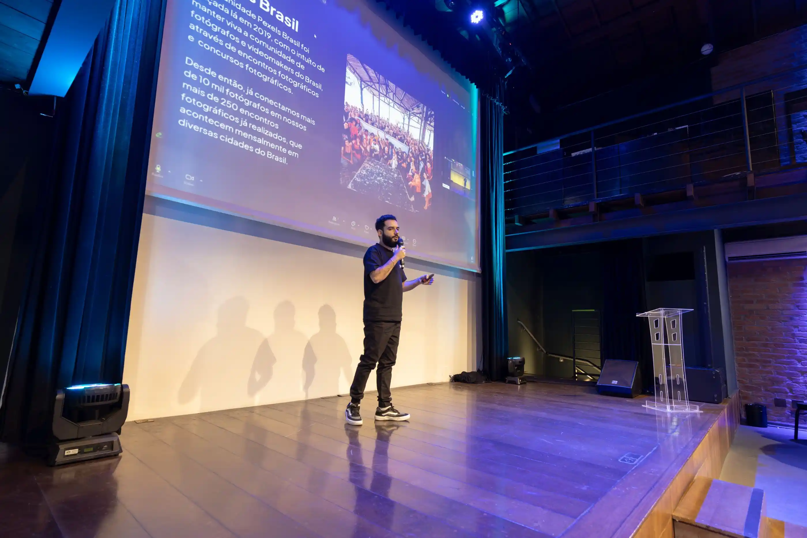 A speaker on stage beside a projected slide in a dark hall