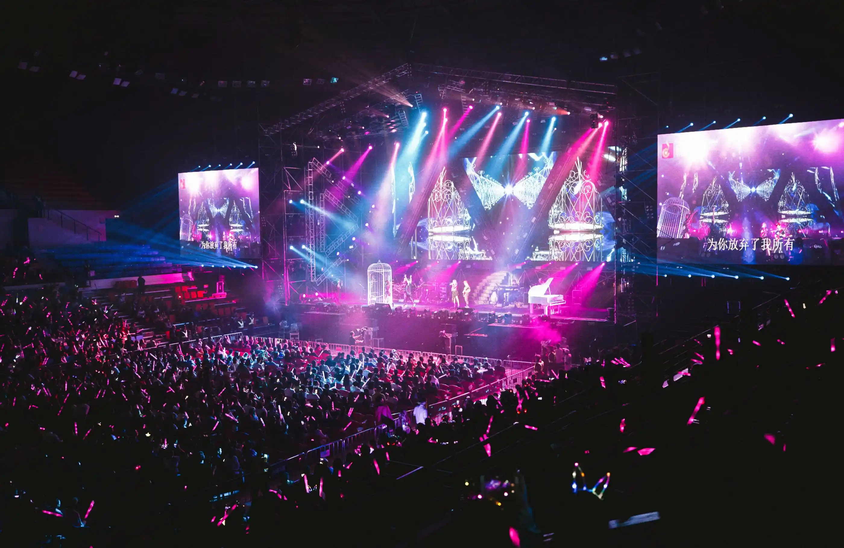 A large crowd in front of a lit stage, screens either side
