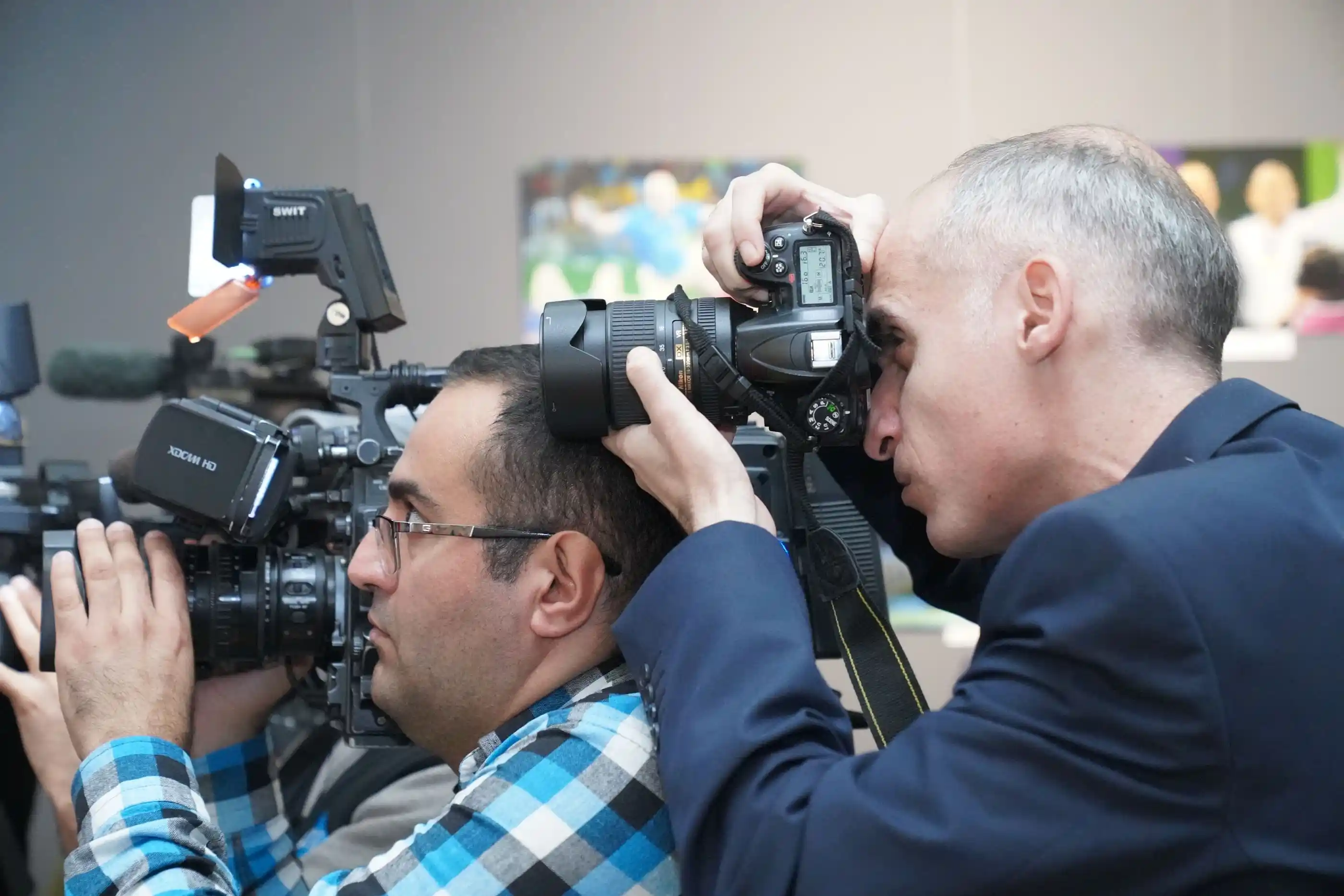 Two photographers shooting an event from the side of the room