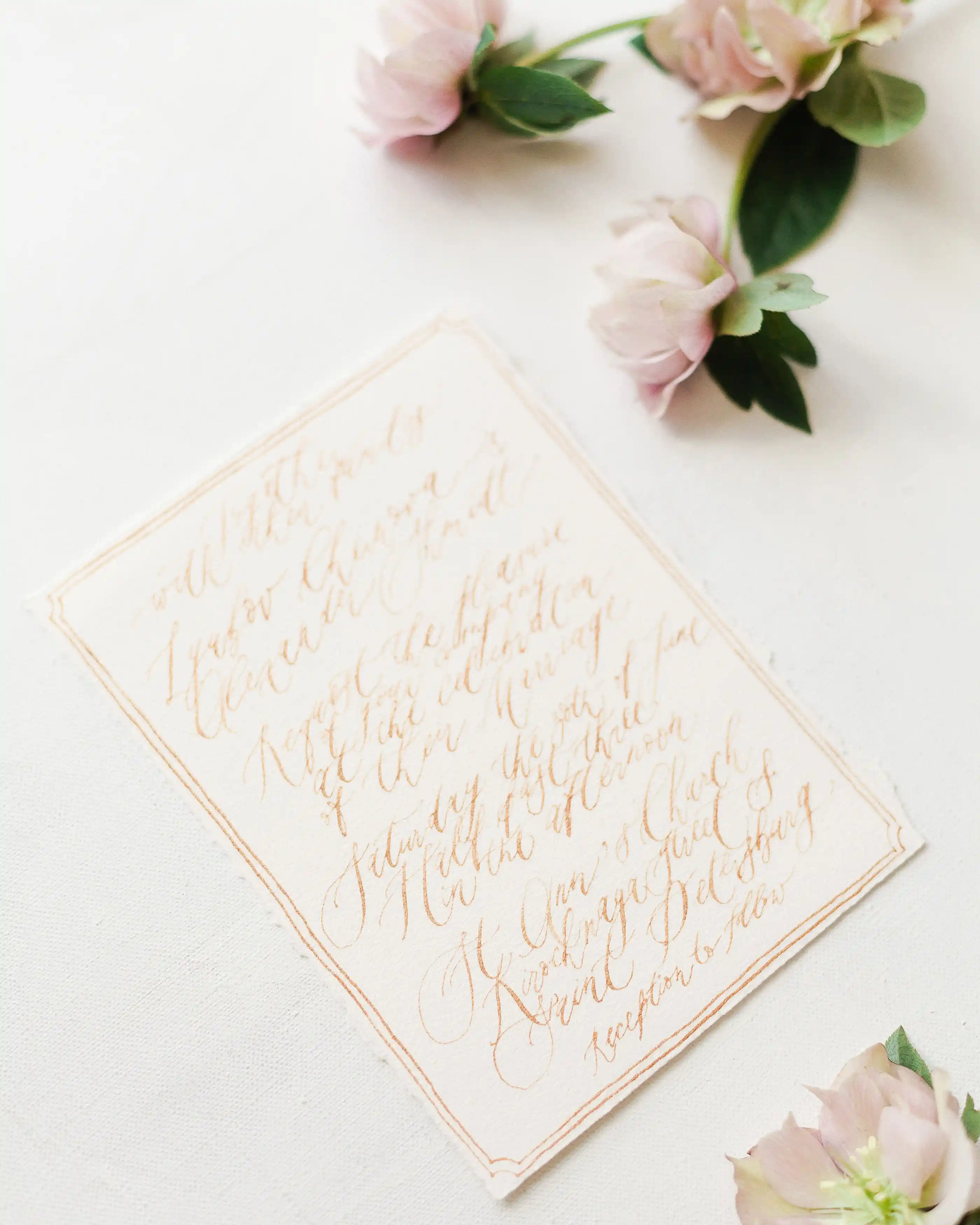 A letterpress invitation card lying beside fresh blooms