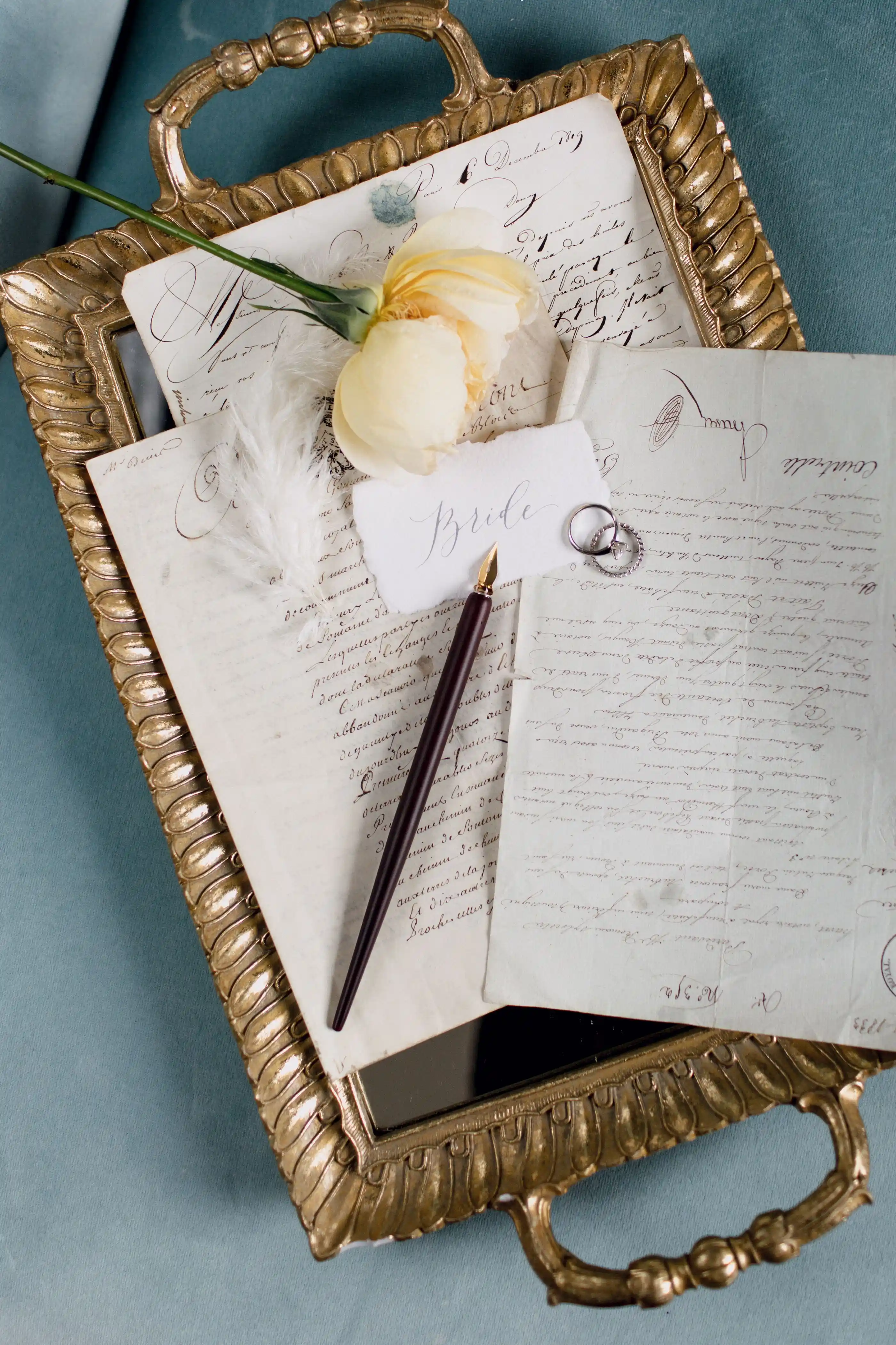 An invitation suite arranged on a gold tray with rings and a pen