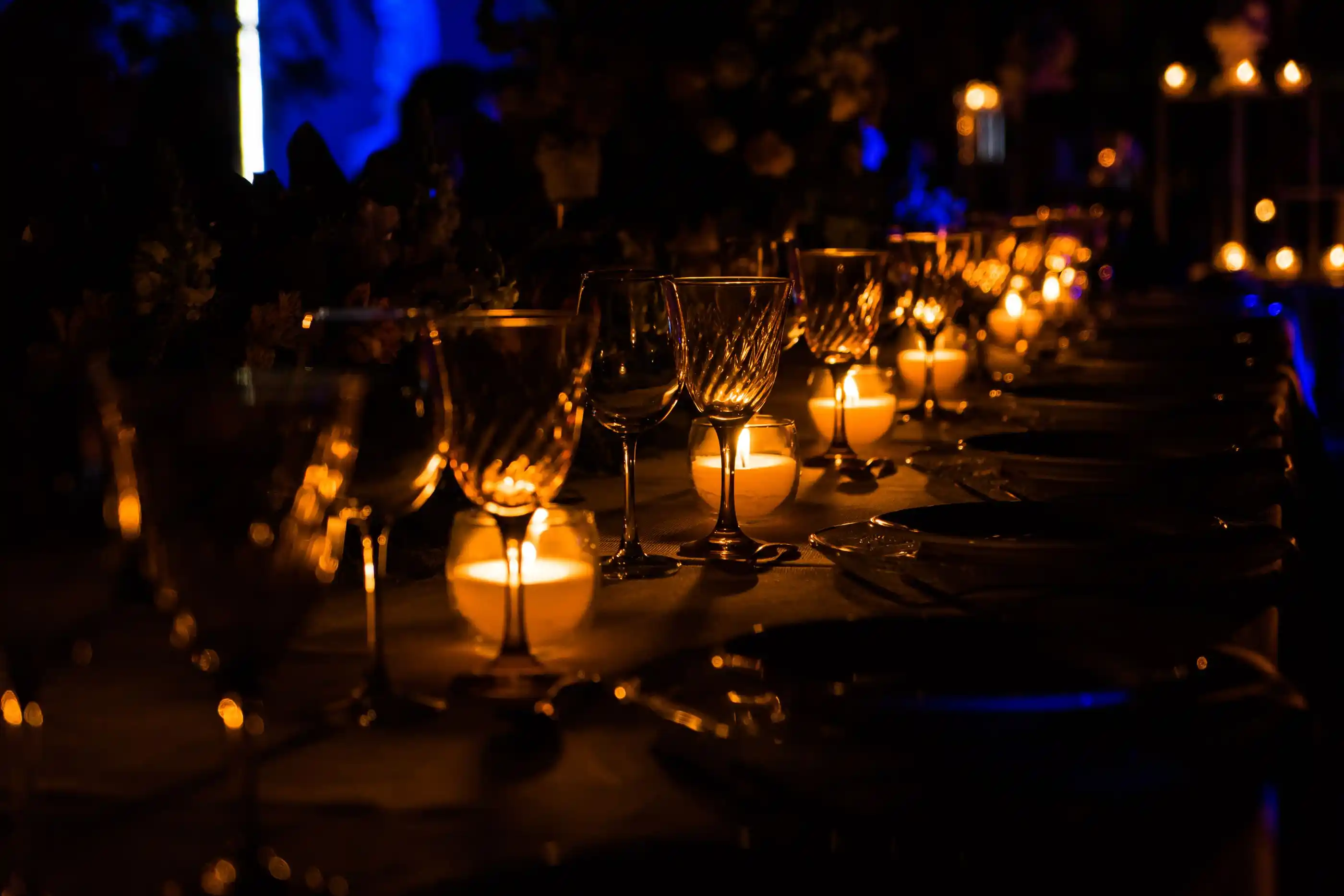 A candlelit table laid with wine glasses in a darkened room
