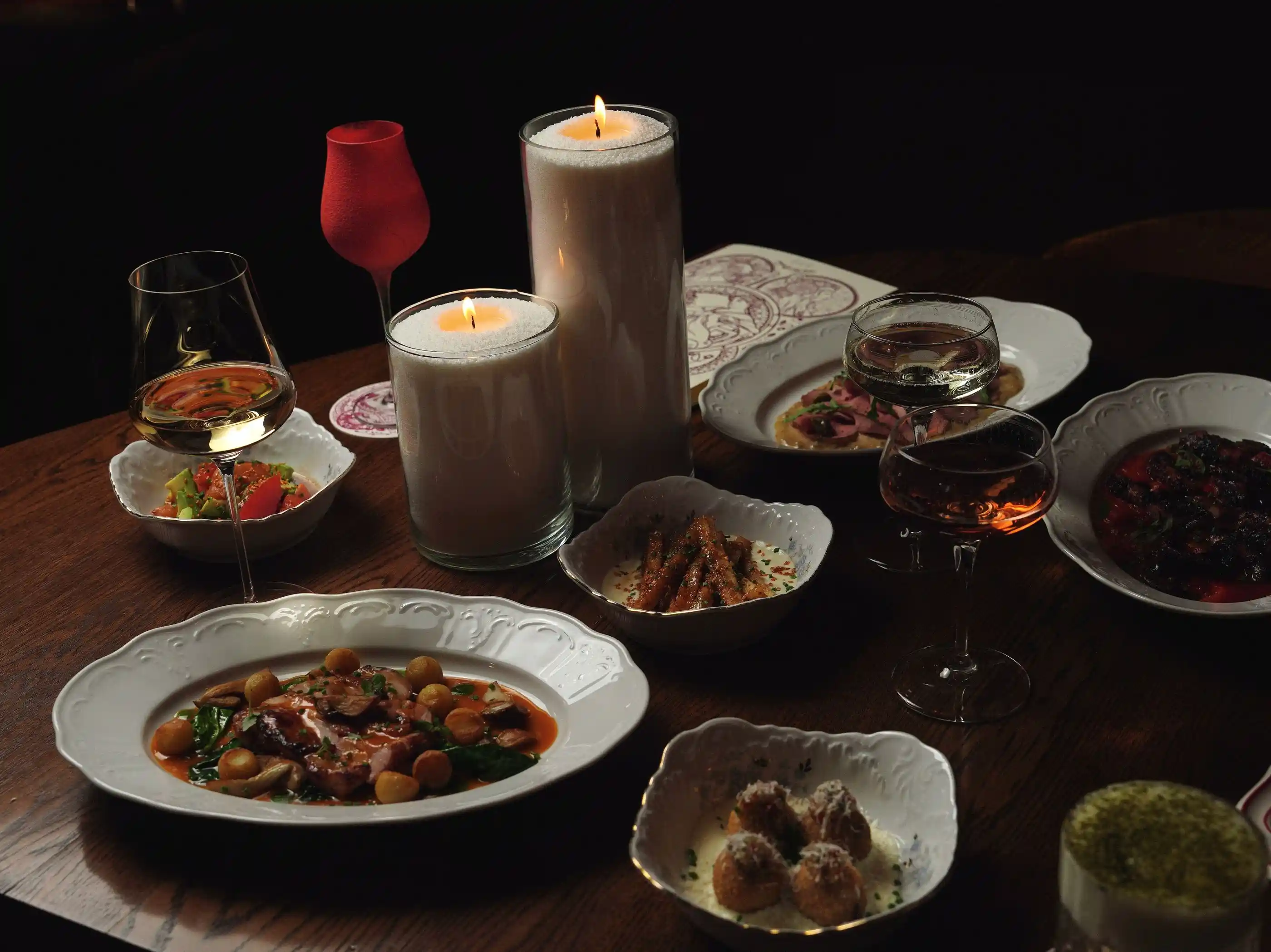 A dinner table of plated courses lit by pillar candles