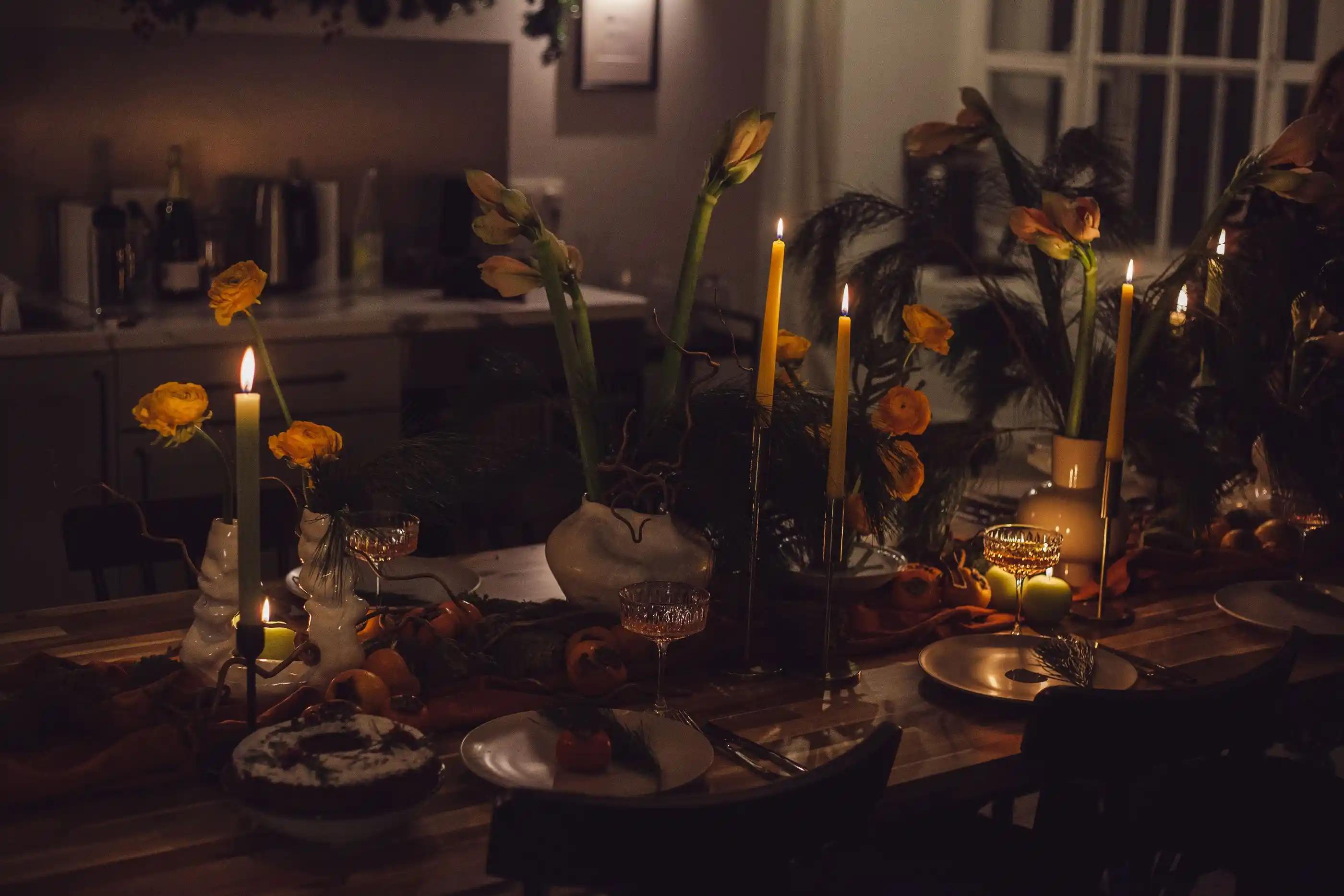 A dining table dressed with candles and low arrangements, warm light from above