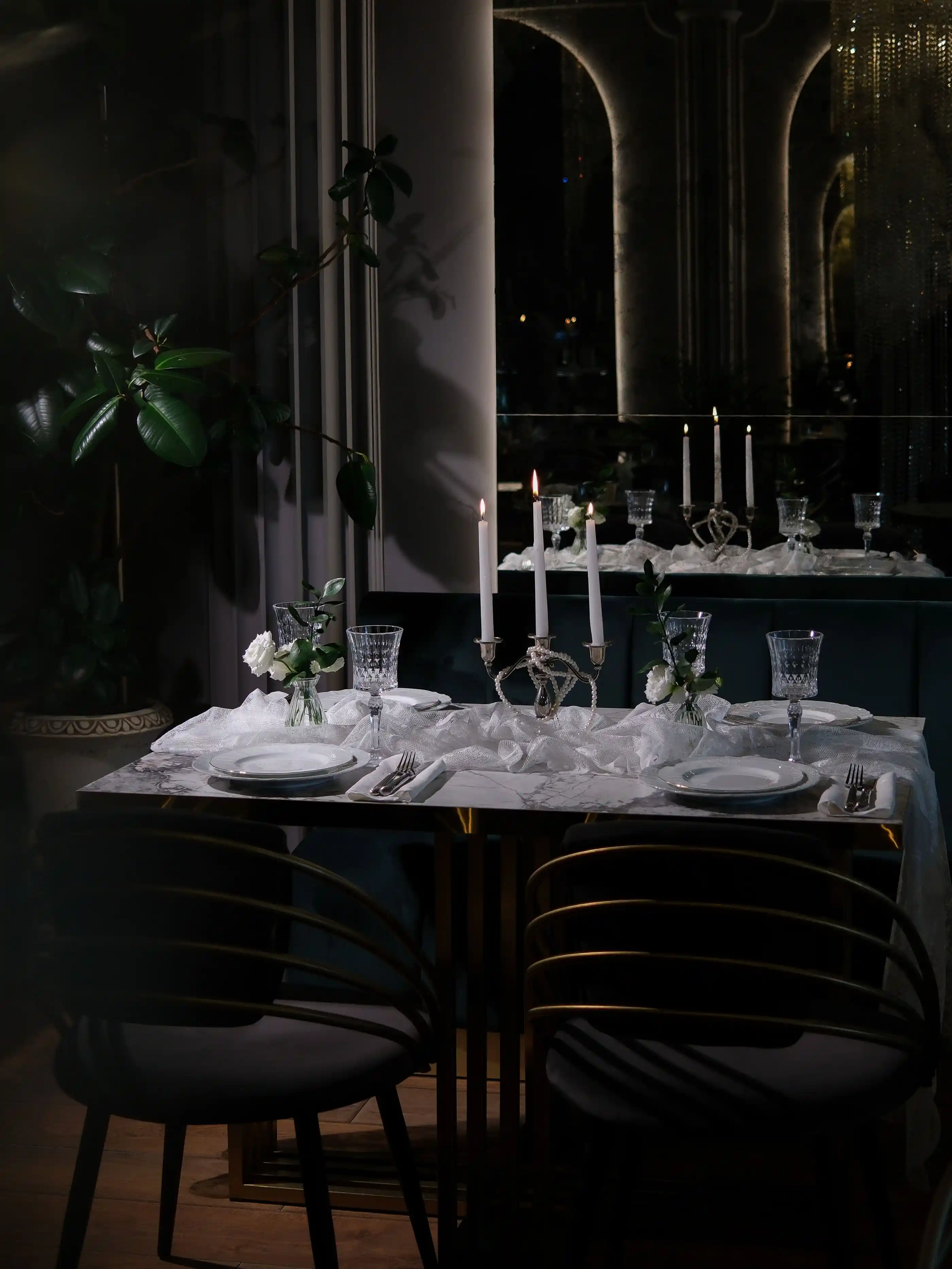A romantic table setting with candles, dark linen and polished glassware