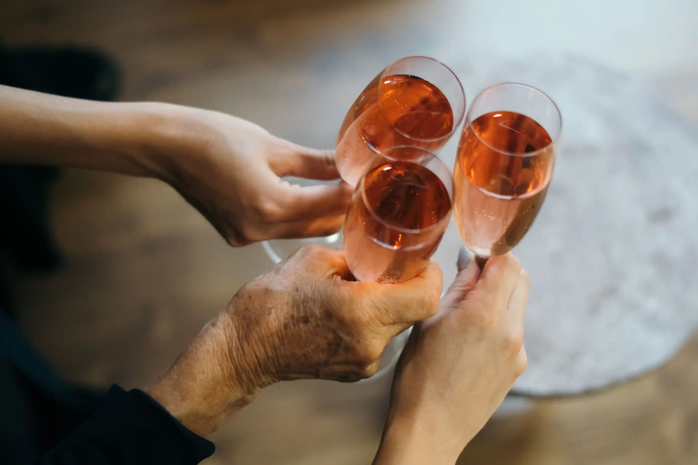 Three hands raising rosé champagne in a toast