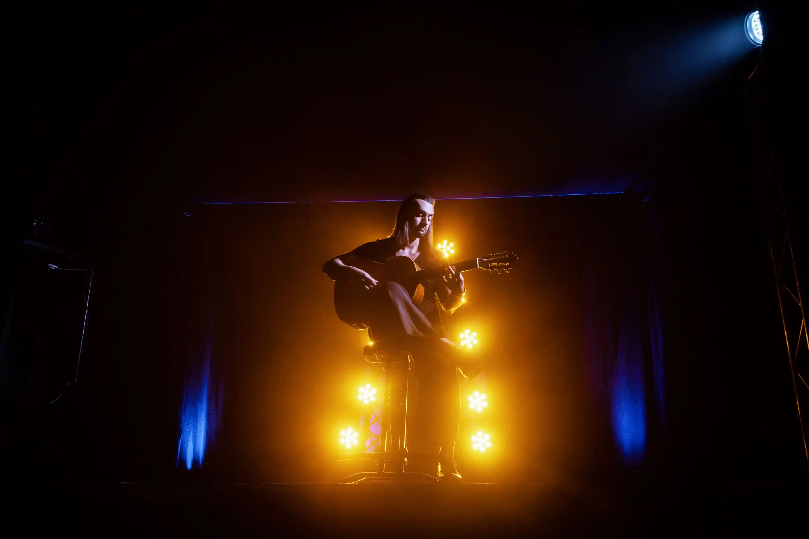 A guitarist performing under a single warm spotlight