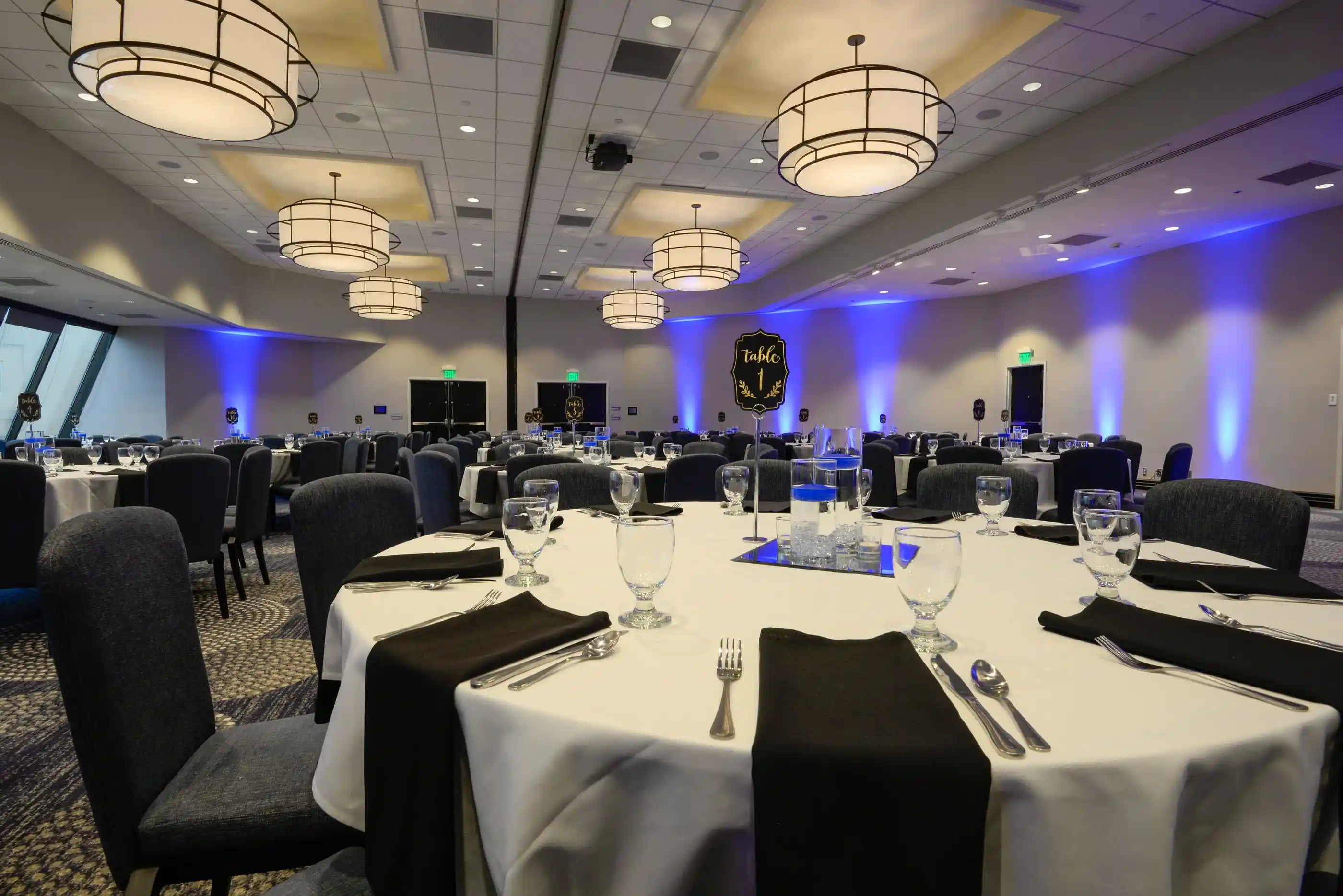 A banquet floor laid with round tables and a lit stage beyond