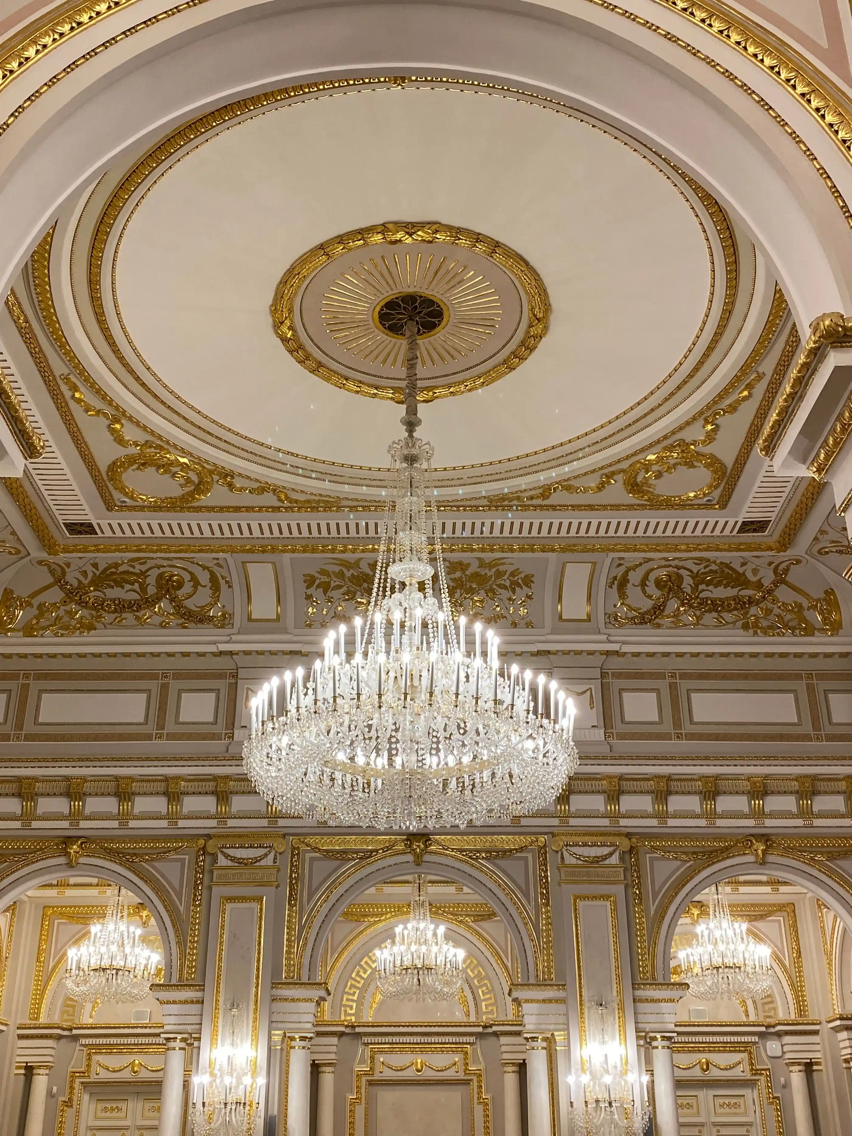 A gilded ceiling and chandeliers seen from the floor below