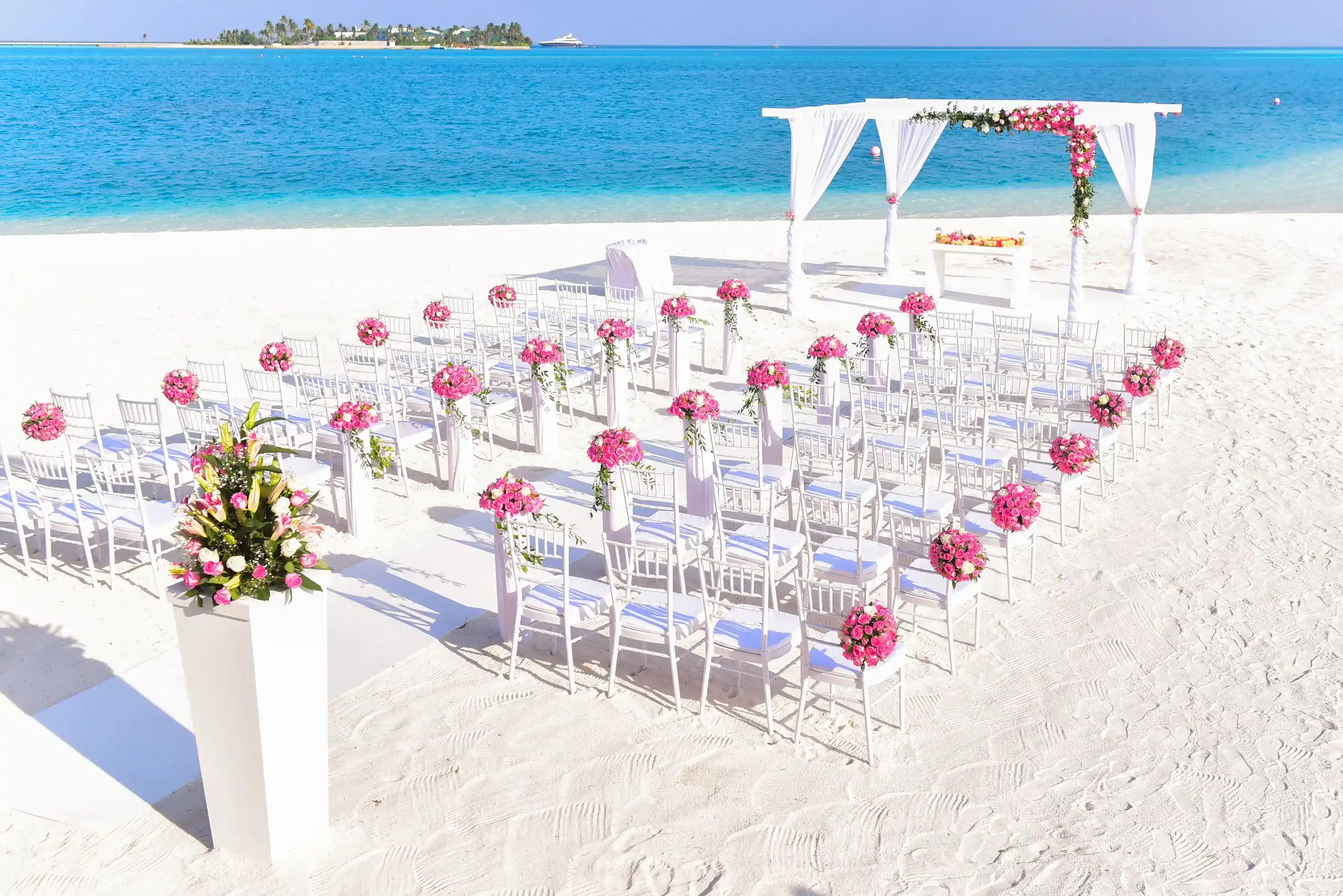A beach ceremony with flowers and an aisle facing open water