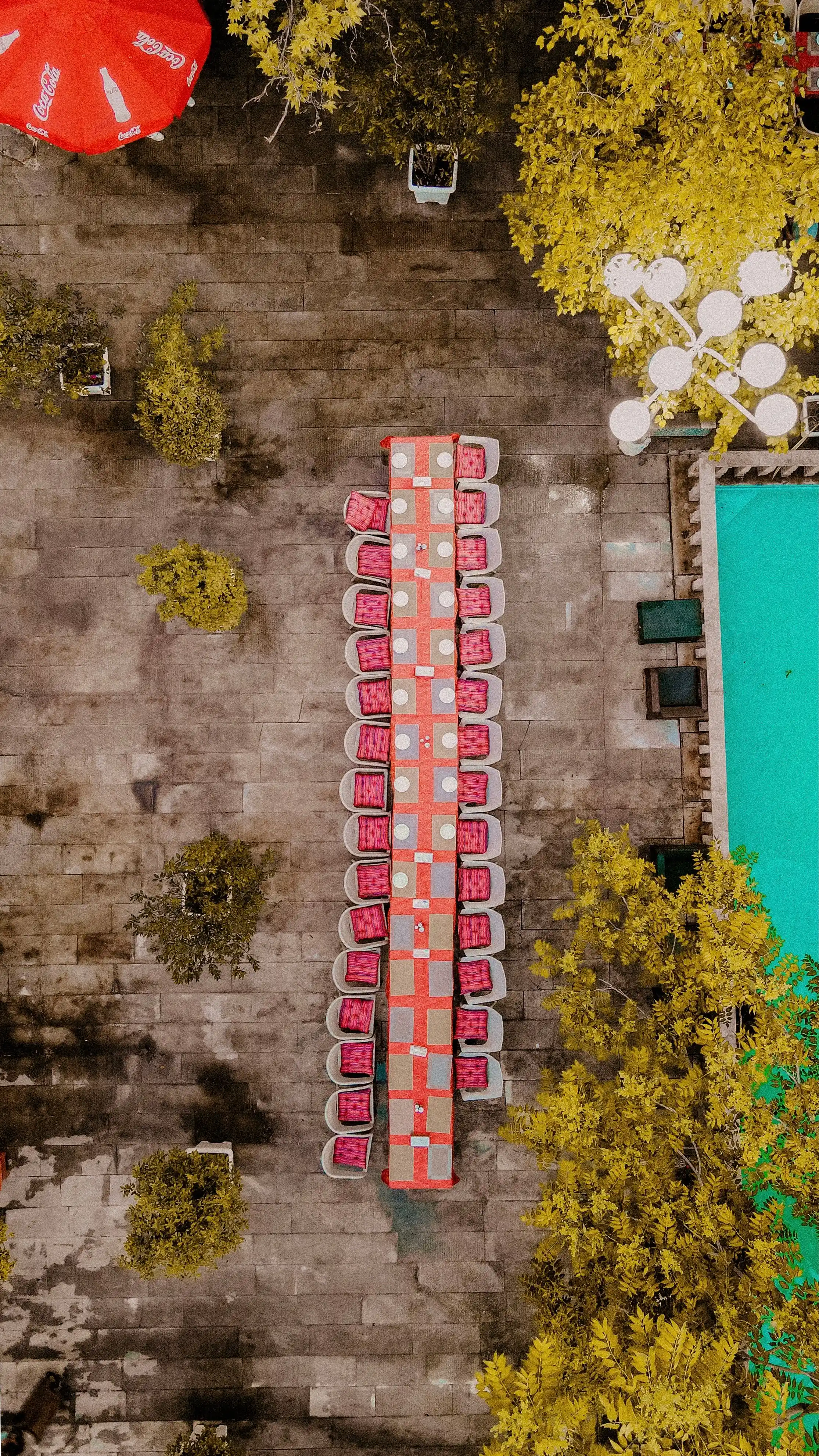 A long dining table beside a pool, photographed from directly above