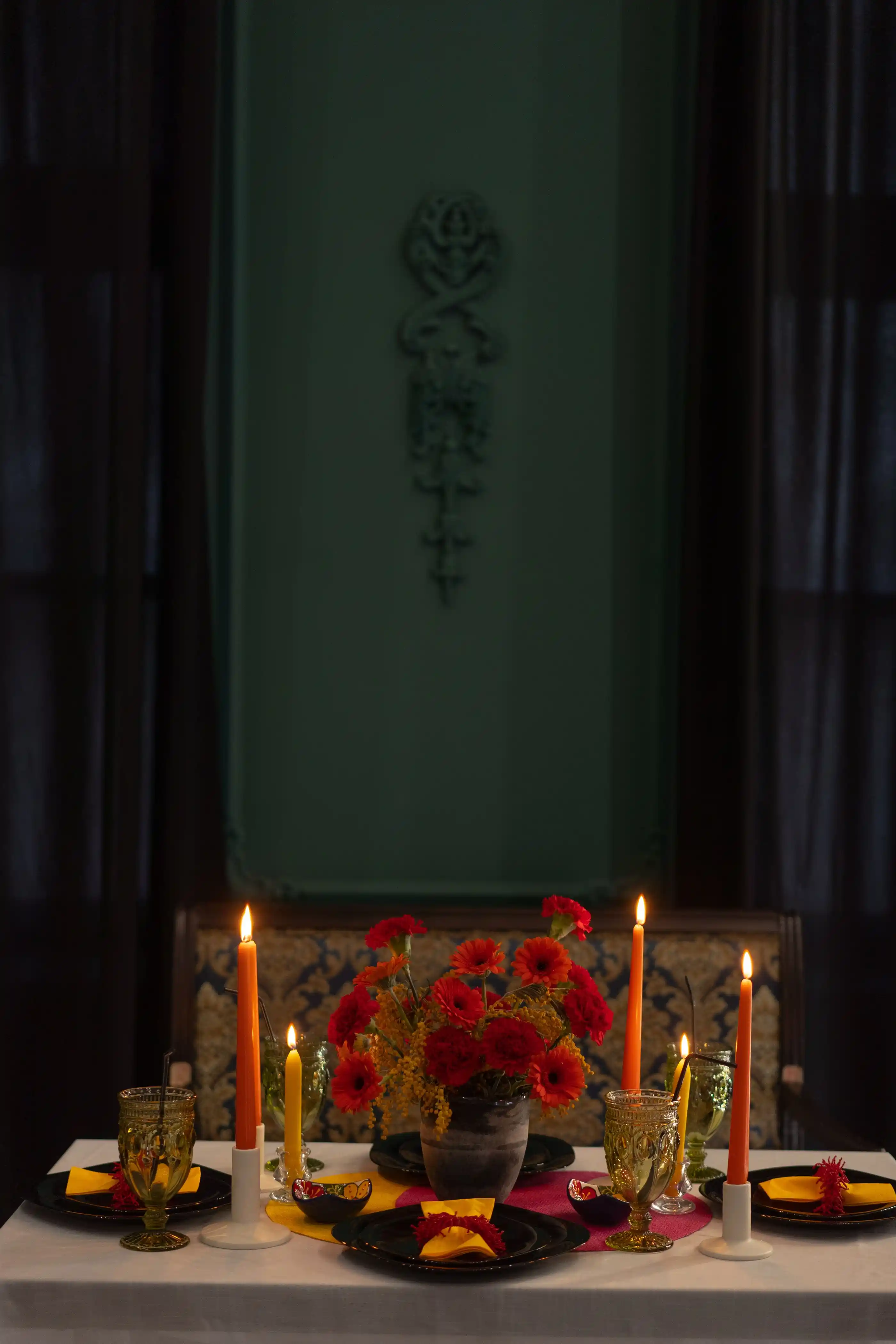 A table styled with tapers and deep red blooms against a green wall