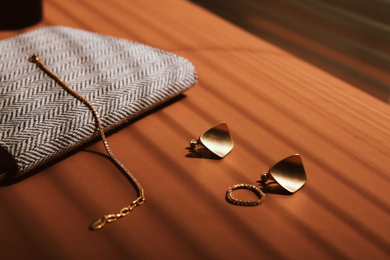 Gold jewellery laid across herringbone cloth in warm evening light