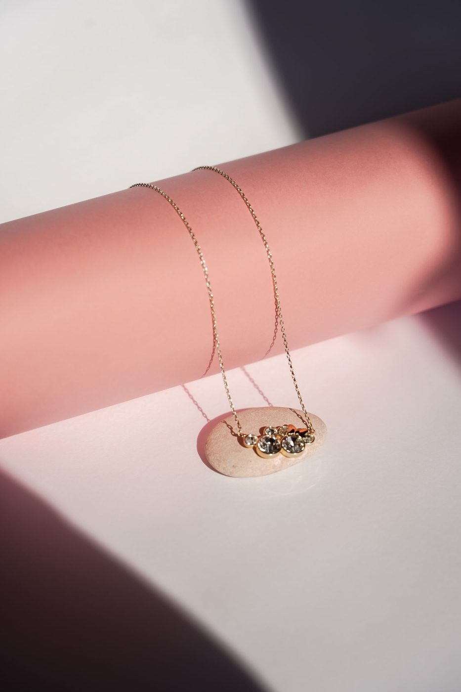 Delicate gold chain necklace draped over a pink paper roll in soft light