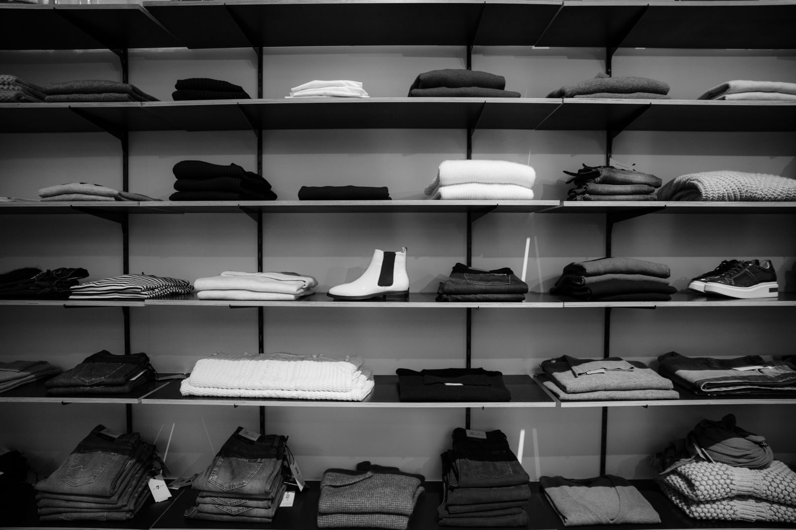 Black and white photograph of folded Eastfold menswear on dark retail shelving