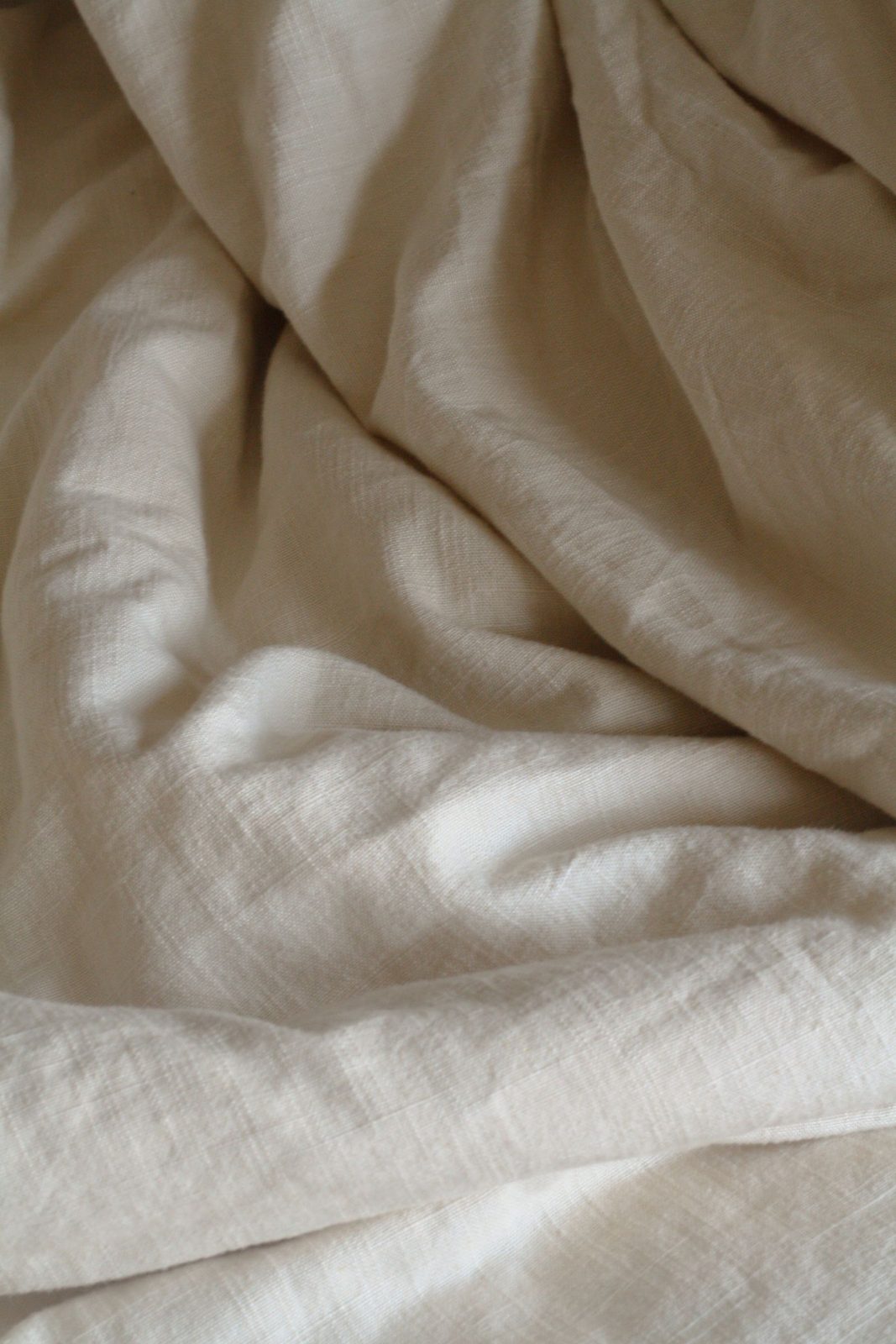 Soft draped natural linen bedding in warm neutral folds for Hartley Linen