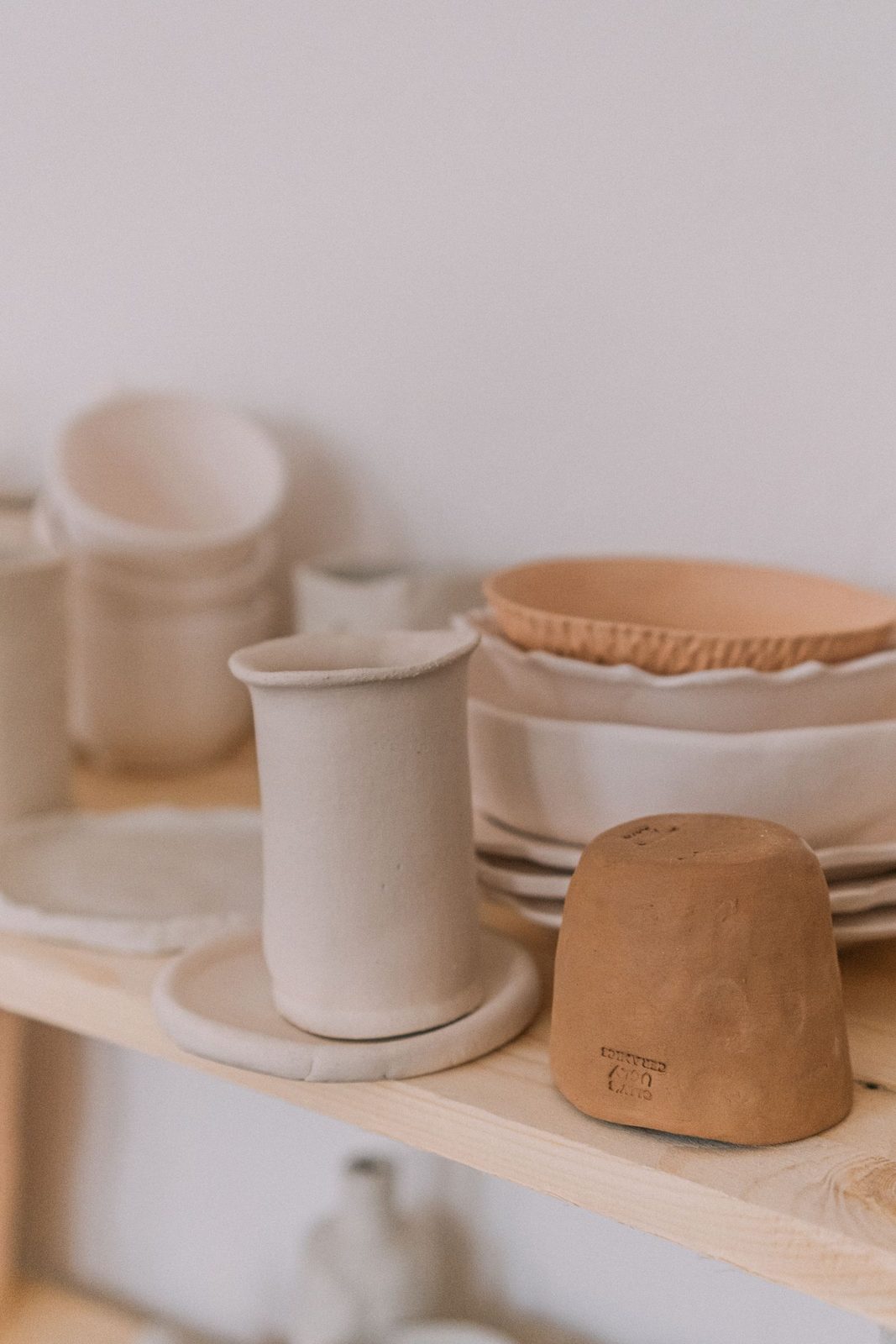 Handmade cream and terracotta ceramics arranged on a wooden shelf for Kiln