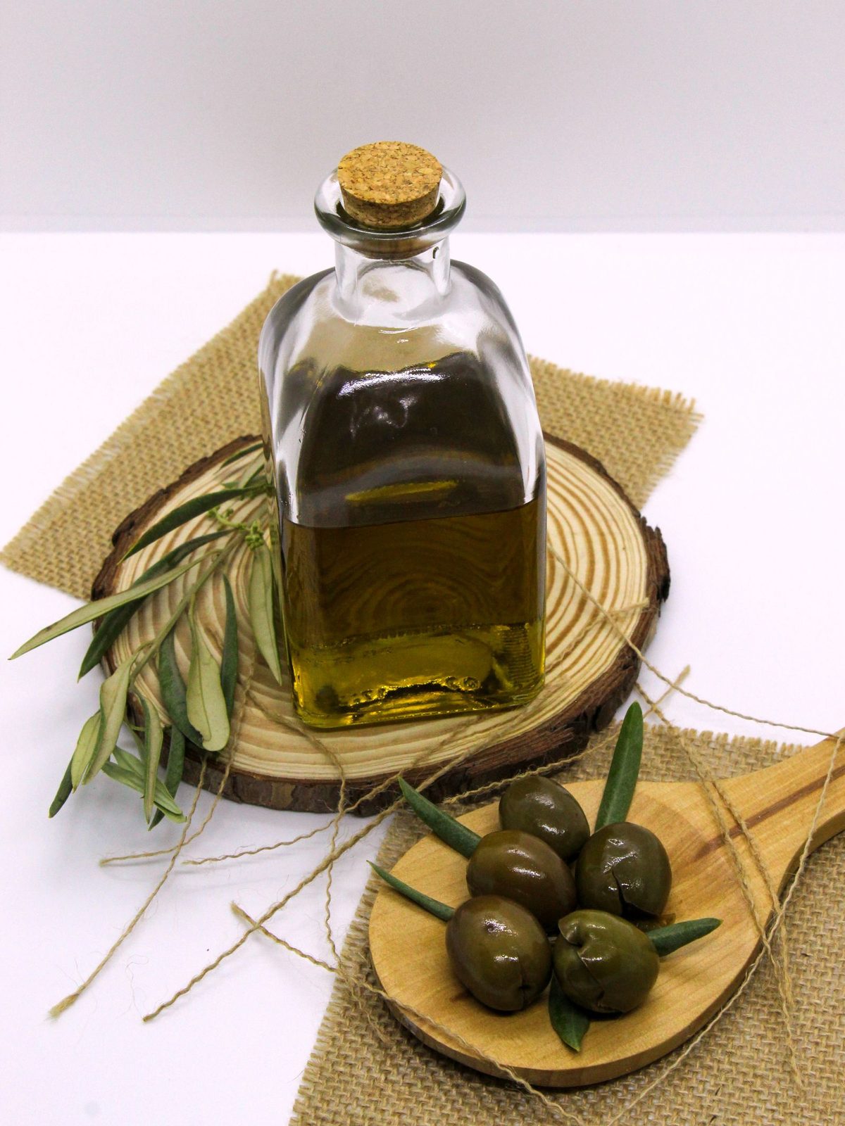 Corked bottle of Oleva olive oil on a wooden board with fresh olives