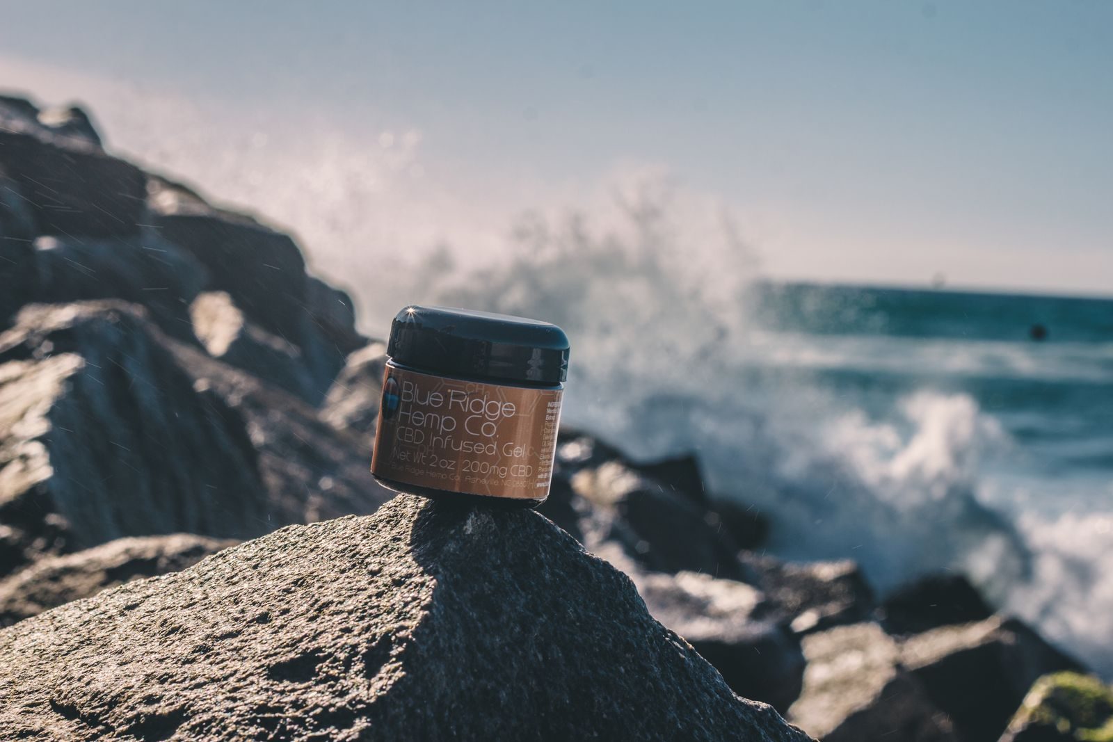 Salt Theory skincare jar photographed on coastal rocks as a wave breaks behind it