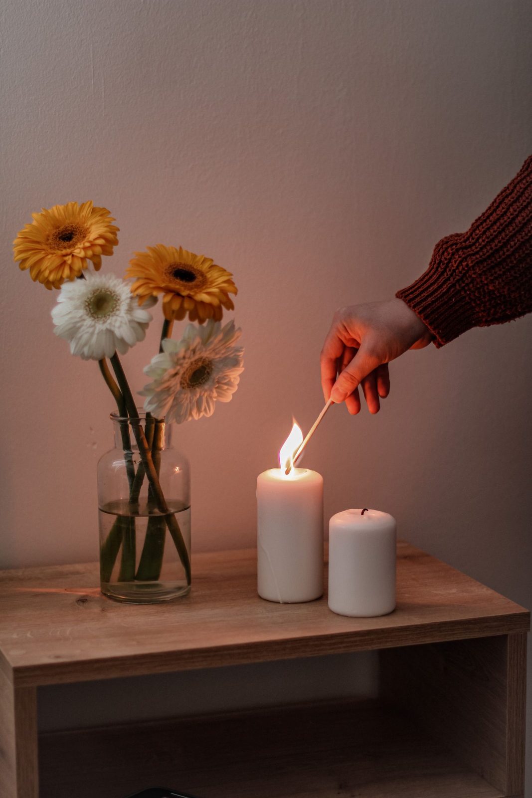 A hand lighting candles beside a vase of flowers during a product styling session