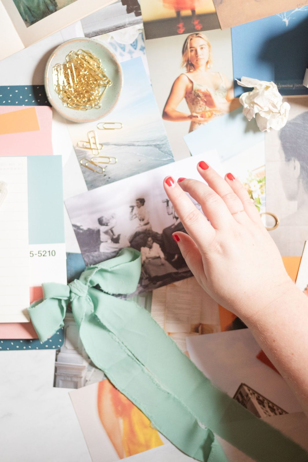 A hand arranging photographs, paint chips and ribbon on a brand moodboard