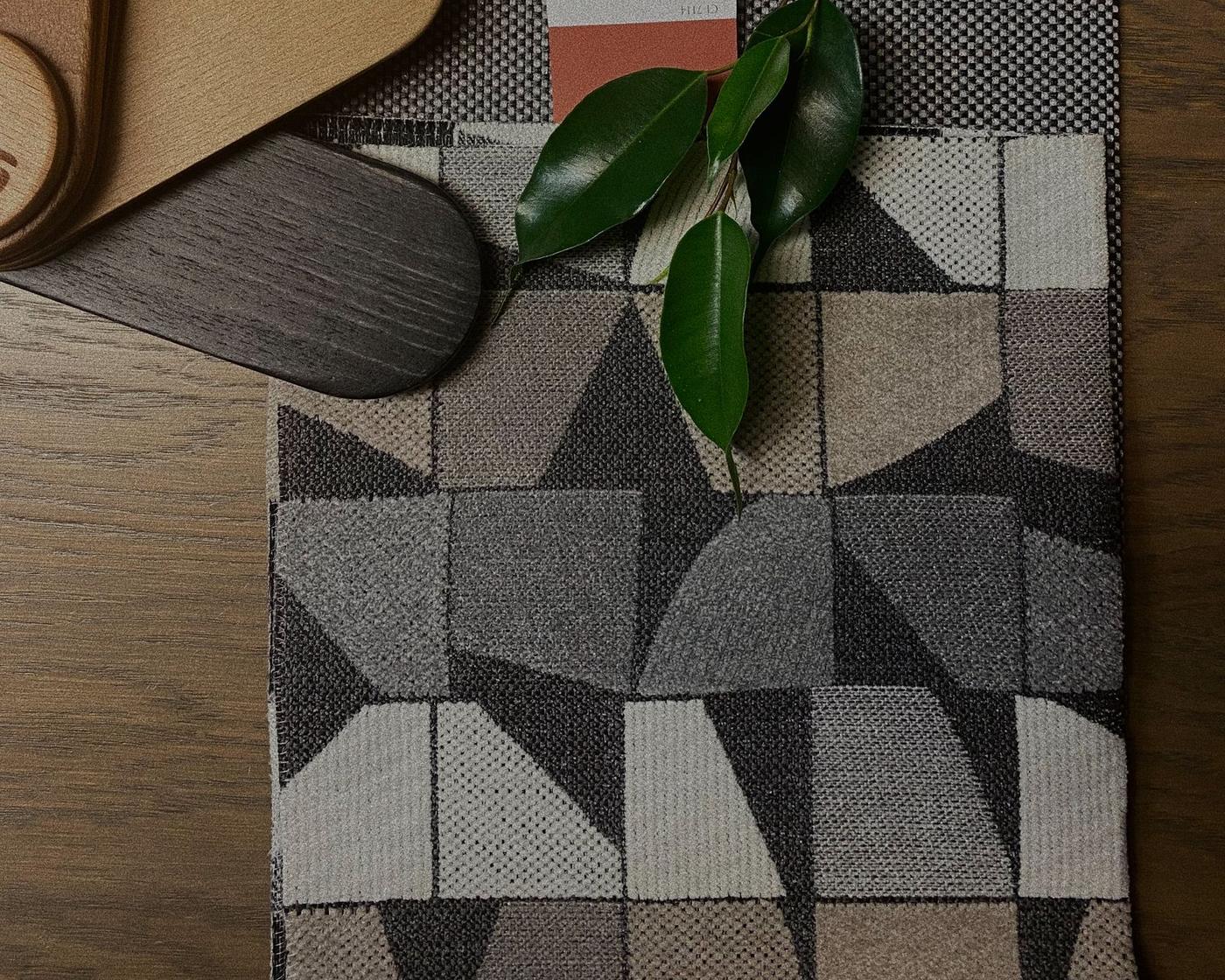 Geometric upholstery textile samples and wood veneers arranged with a magnolia stem