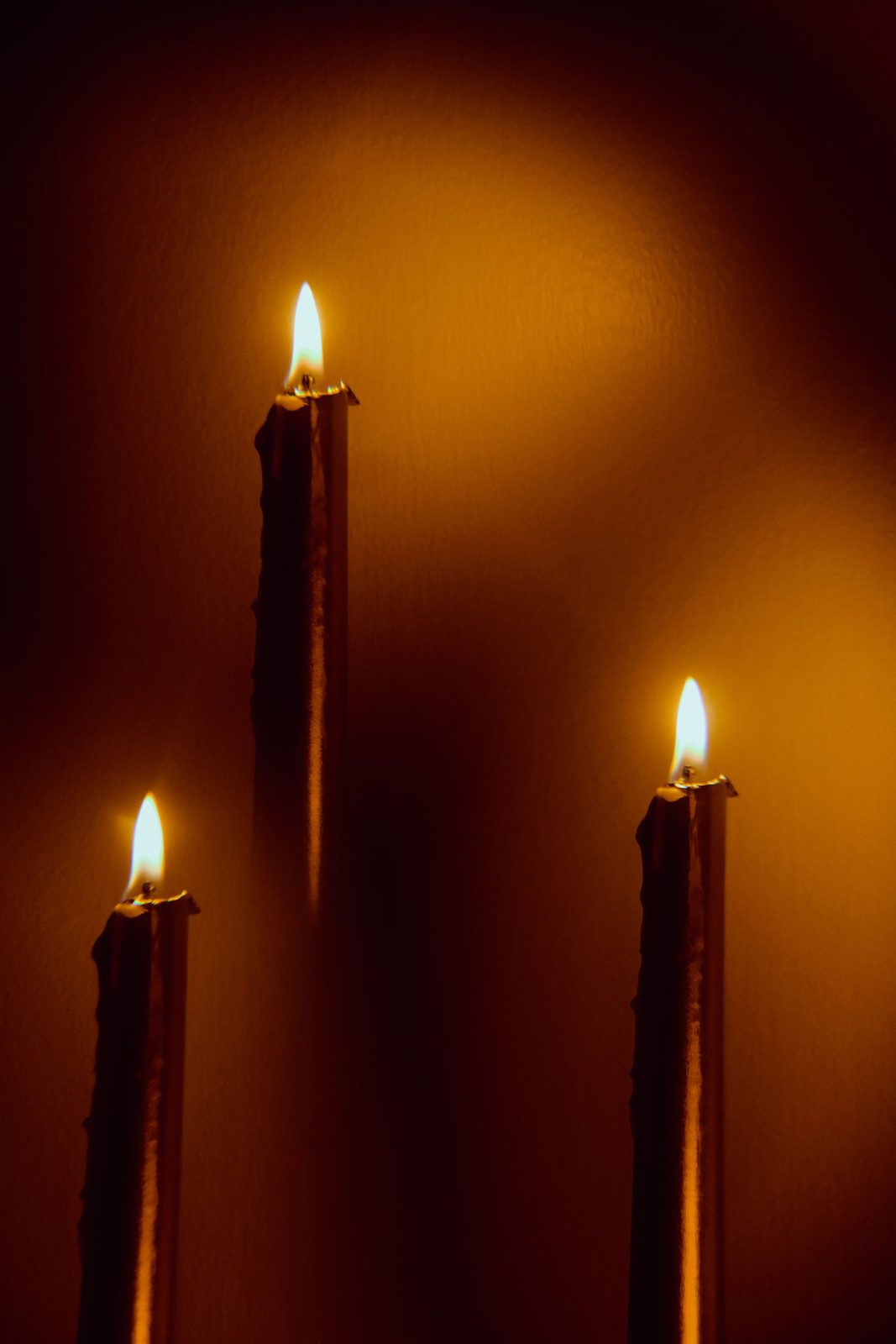 Three hand-dipped taper candles burning against a dark amber backdrop