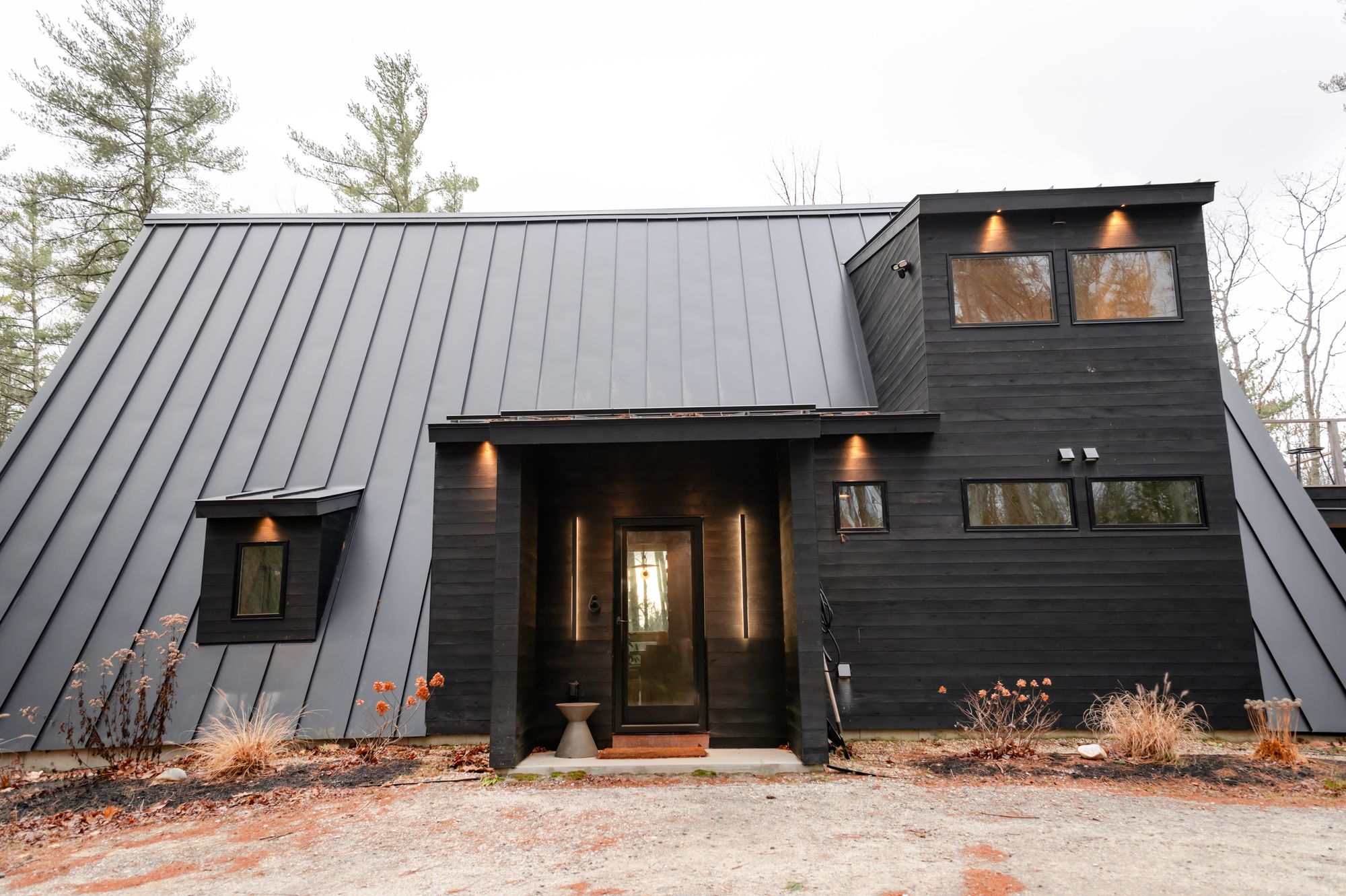 Exterior render of a black A-frame forest retreat with a standing-seam metal roof