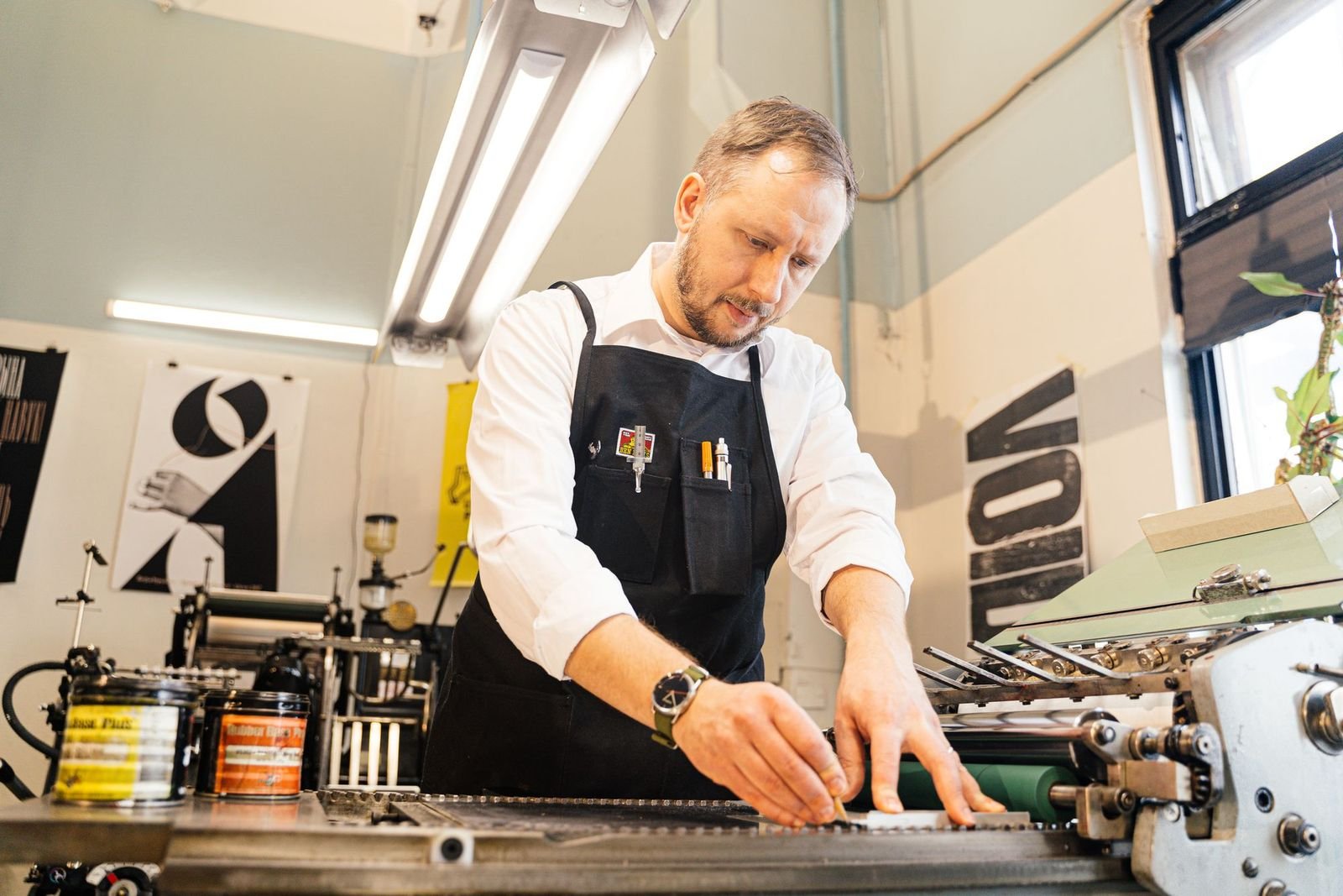 A printmaker pulling a proof at a press in a daylit workshop