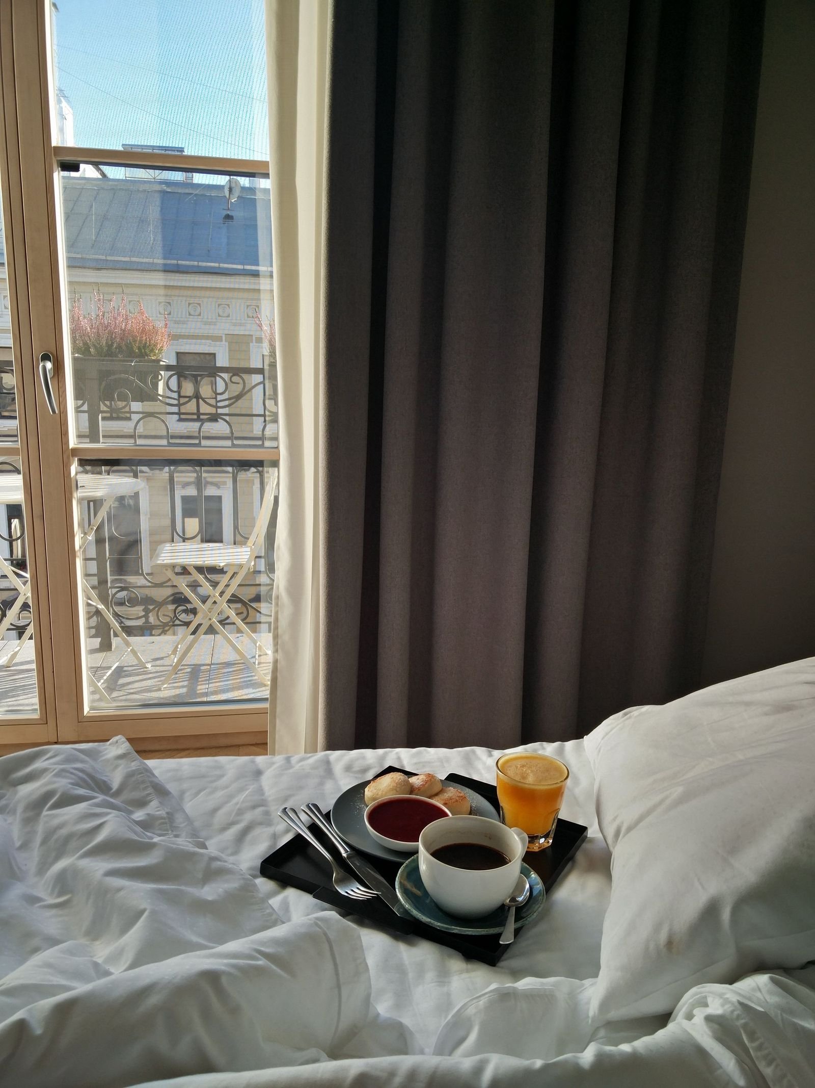A breakfast tray set on a bed beside a window open to the morning