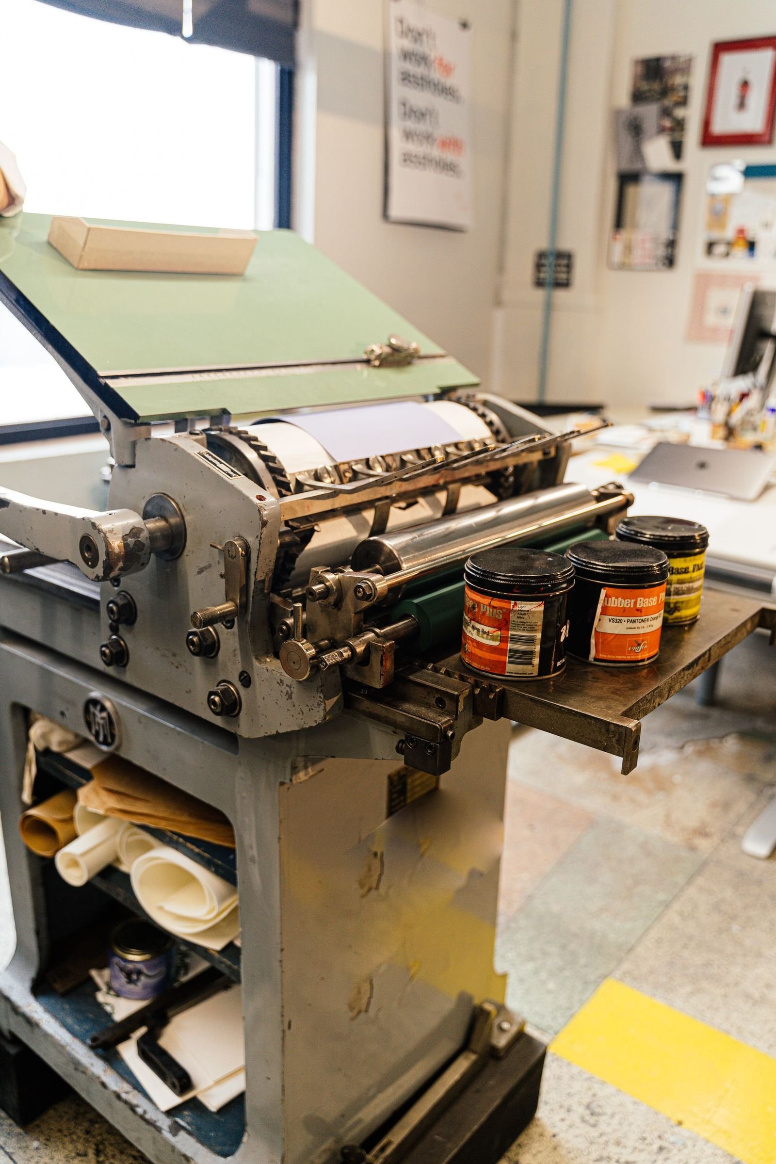 A cast-iron press at rest beside open tins of mixed ink
