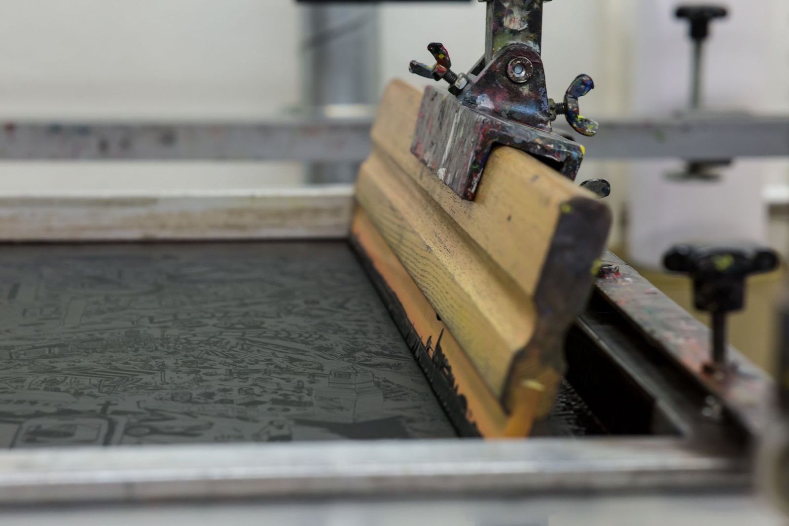 A screen-printing bed with a wooden squeegee resting on the mesh