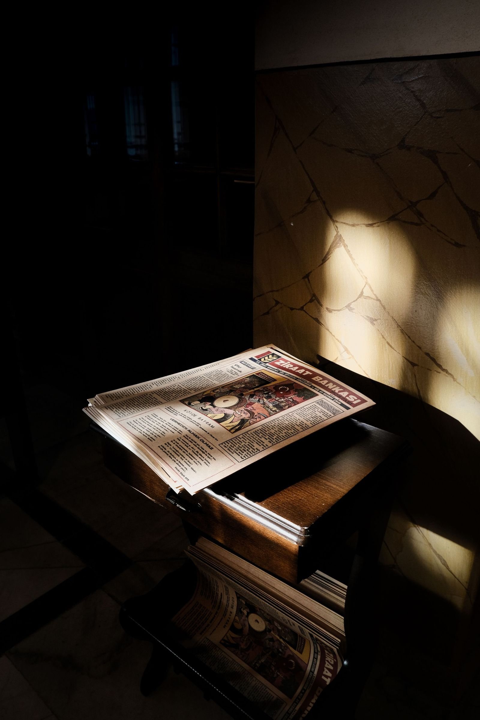 A newspaper on a wooden table in a hard shaft of morning sun