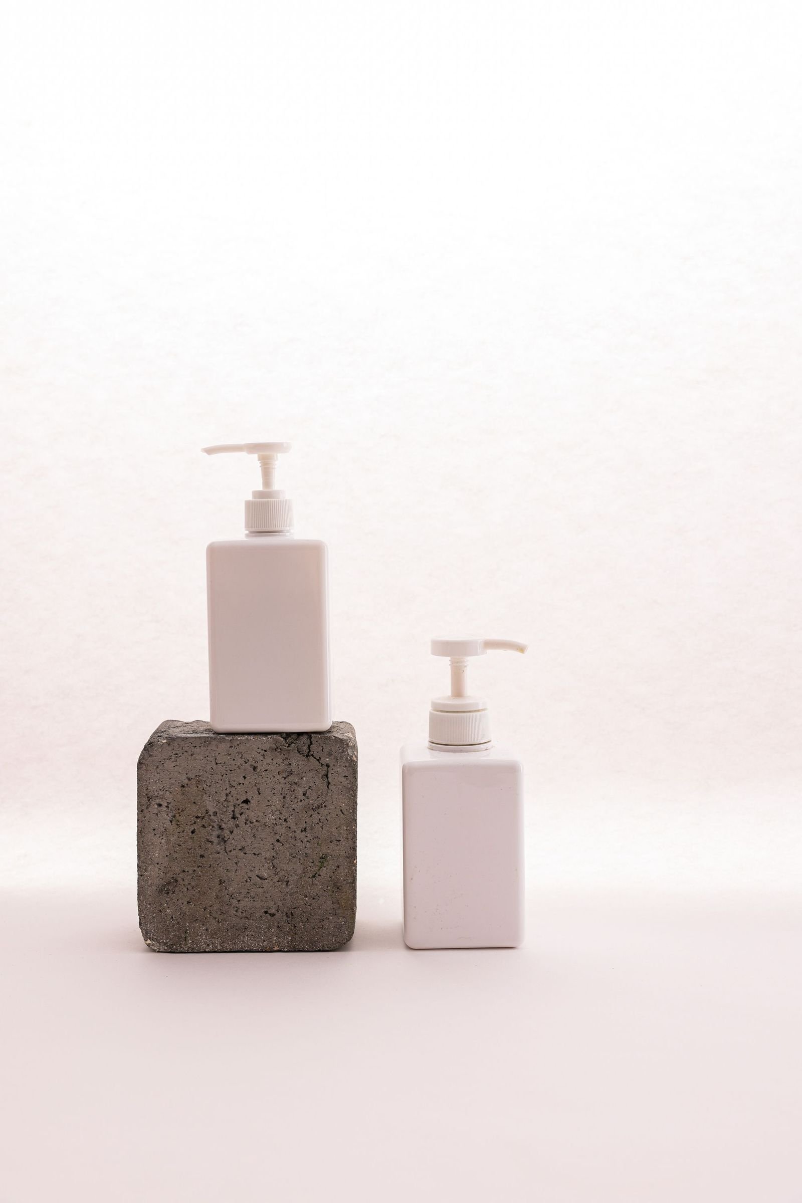 Two unlabelled pump bottles standing on a slab of textured stone