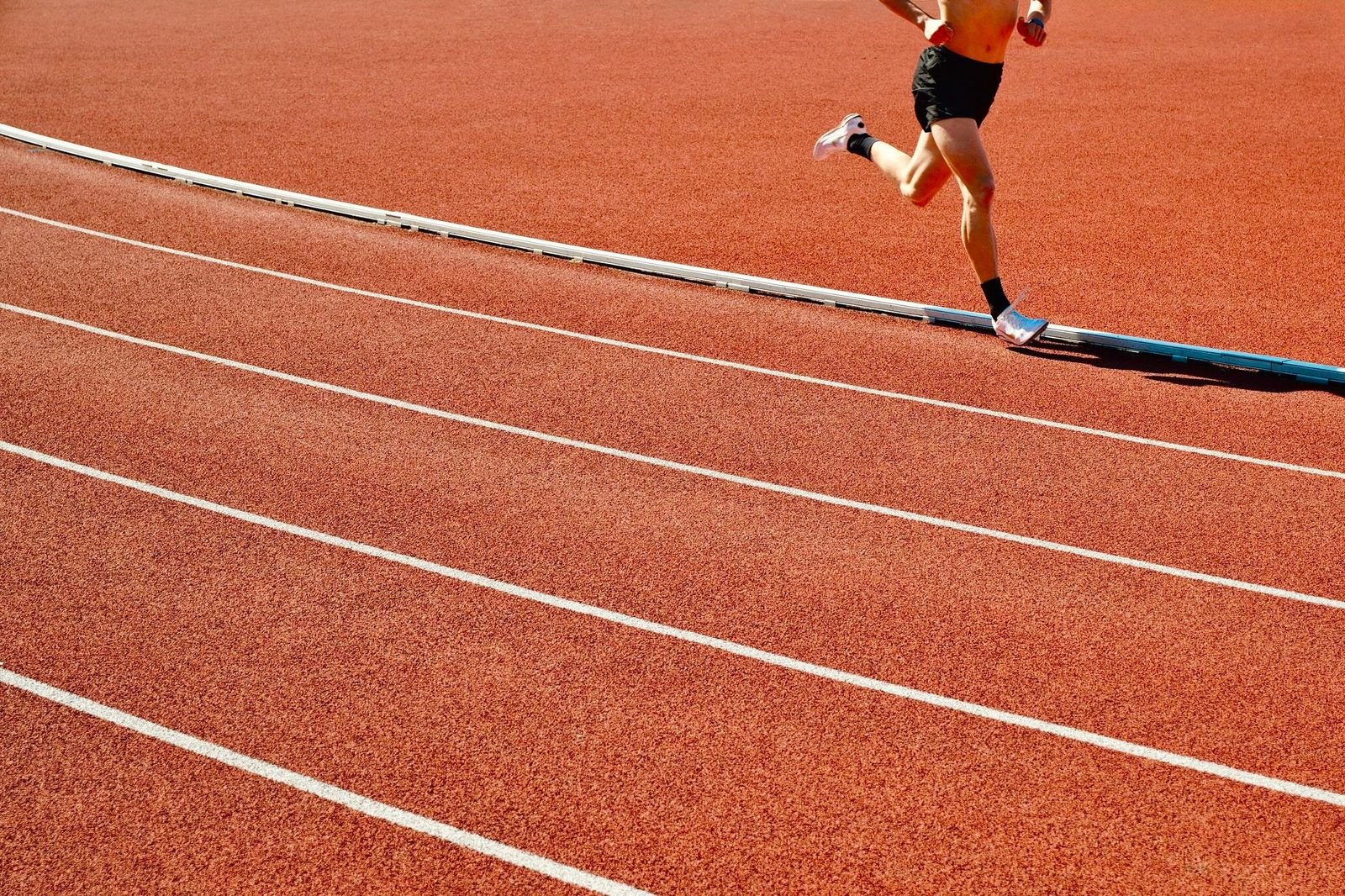 A lone athlete running the outside lane of a red stadium track
