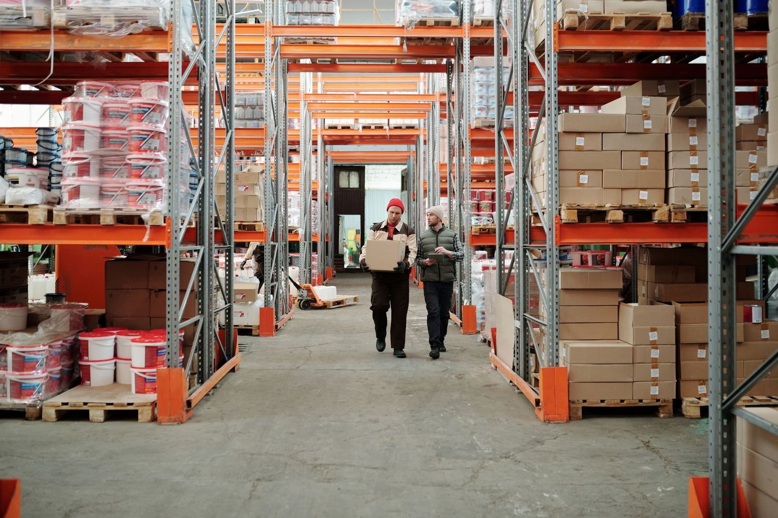 Two workers passing a carton across a wide aisle of pallet racking