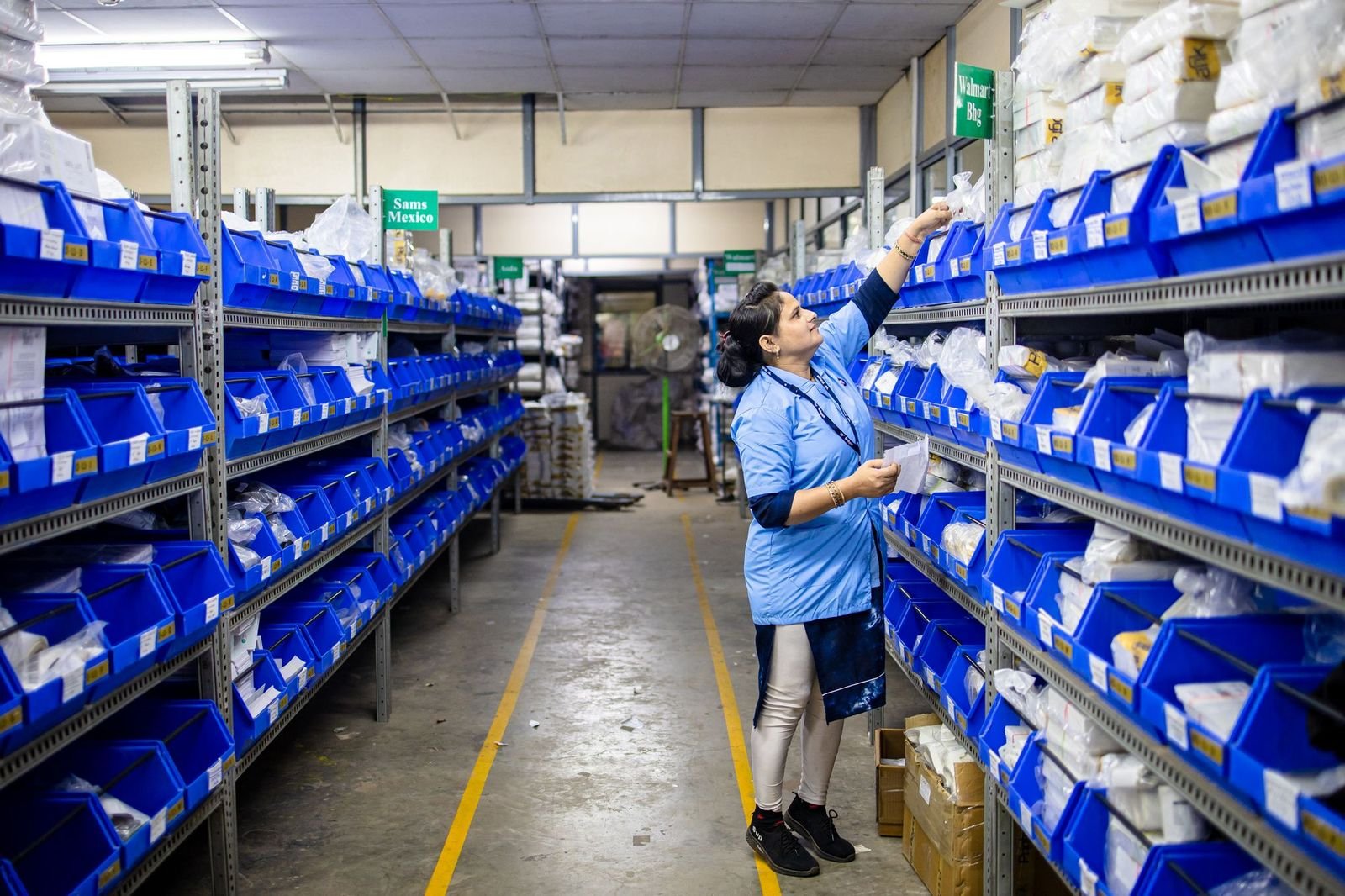 An operator refilling labelled bins along a warehouse aisle