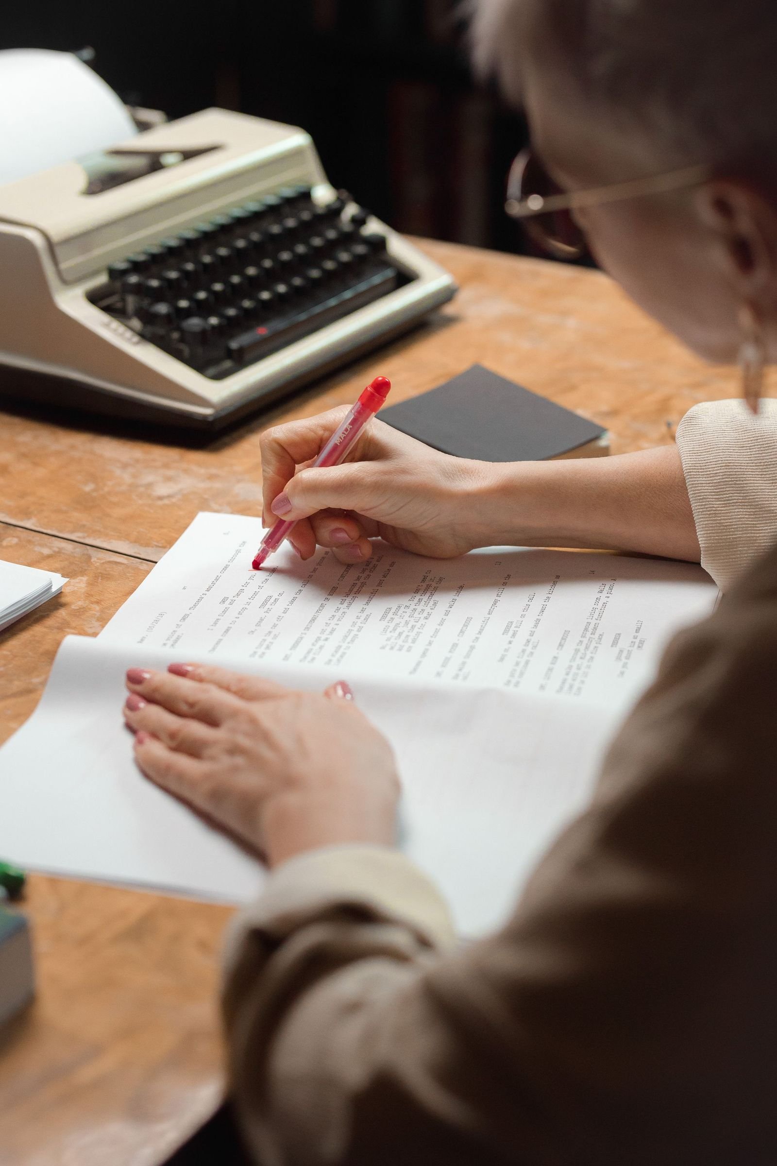 Printed pages being marked up with a red pen beside a typewriter