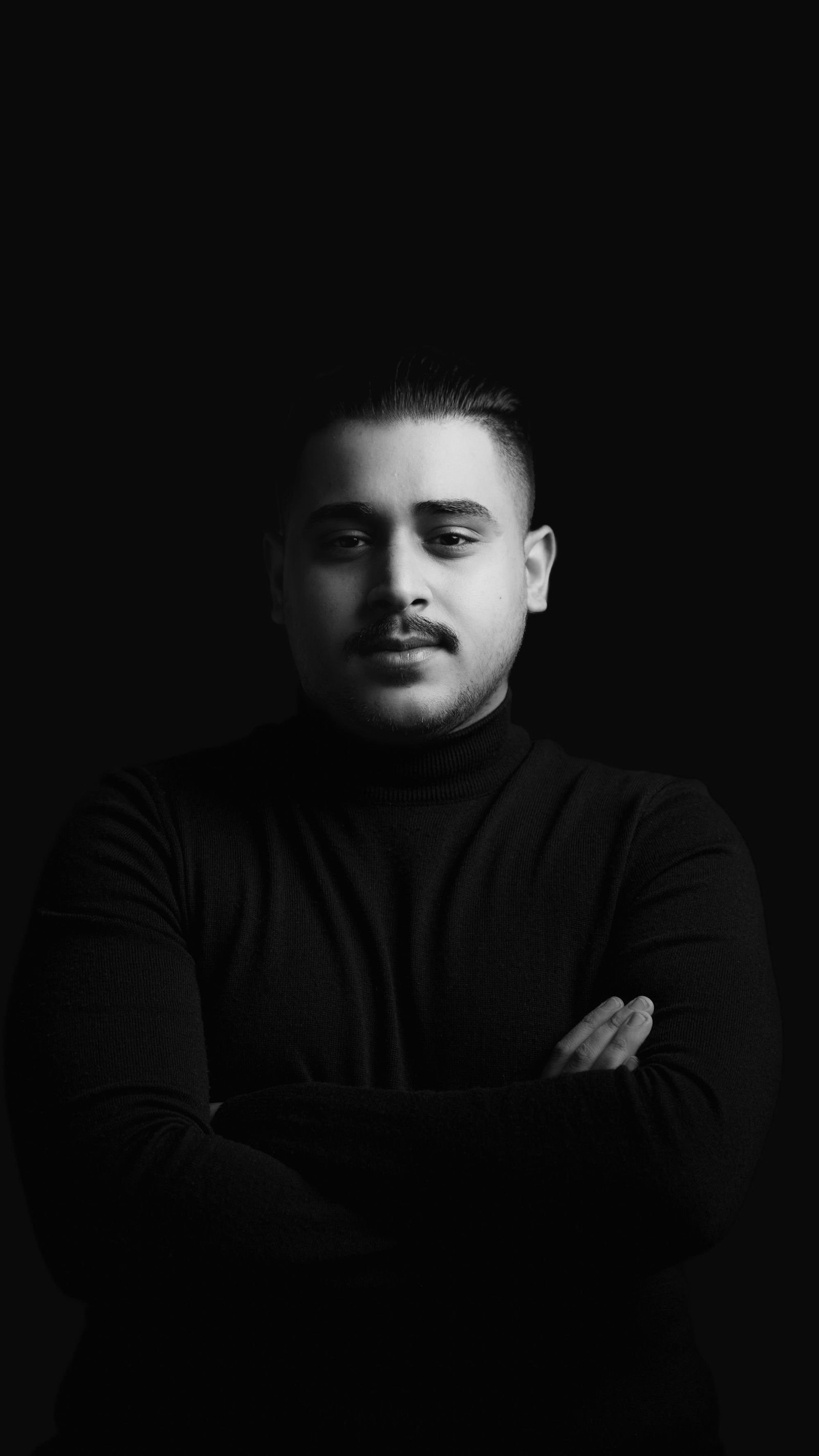 Studio portrait against a dark ground, arms folded