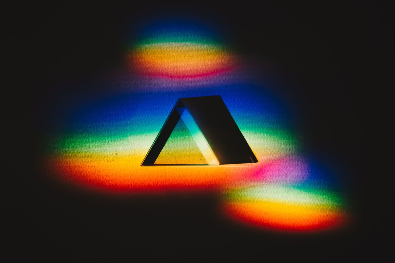 A triangle of light dispersing into a full spectrum on black