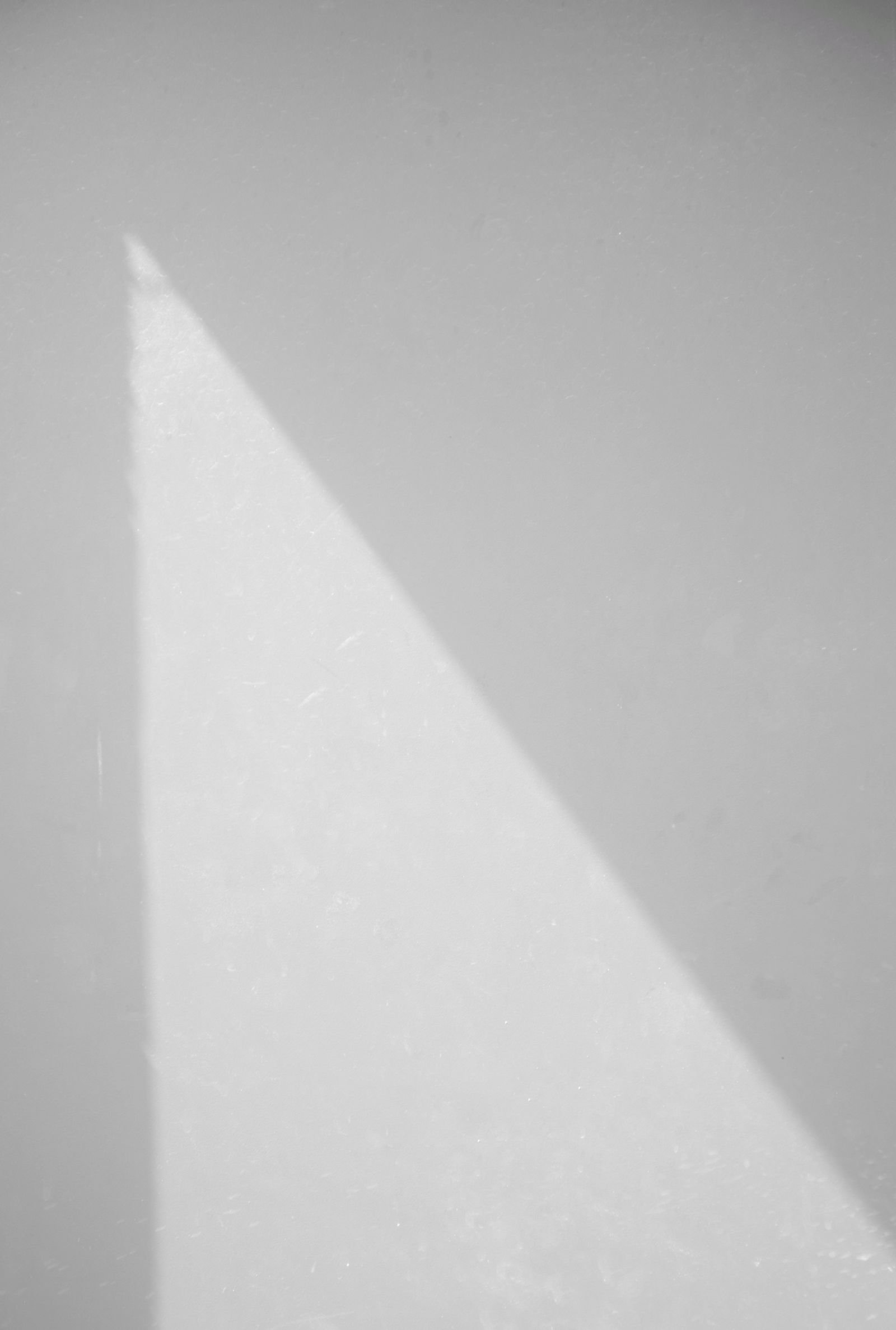 A hard triangular shadow falling across a plain white wall