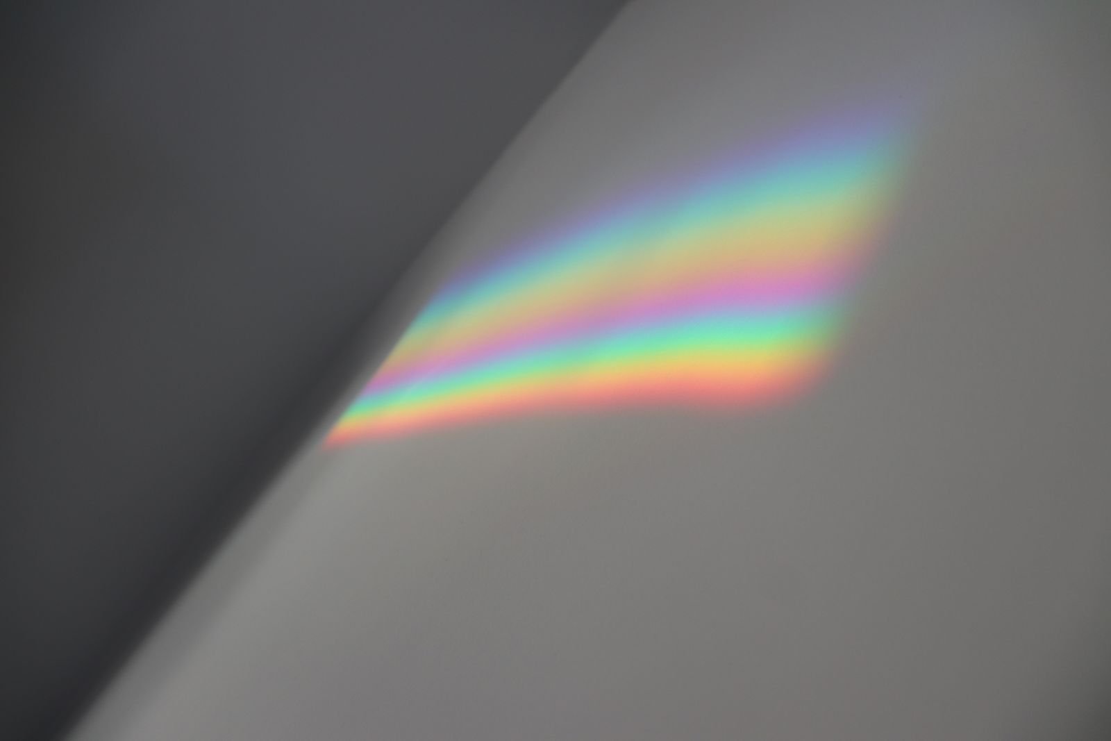 A soft band of refracted spectrum light falling across a grey wall