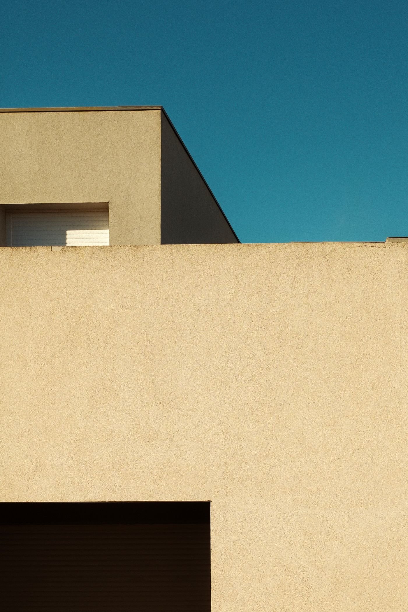A geometric building corner in ochre and cream against blue sky