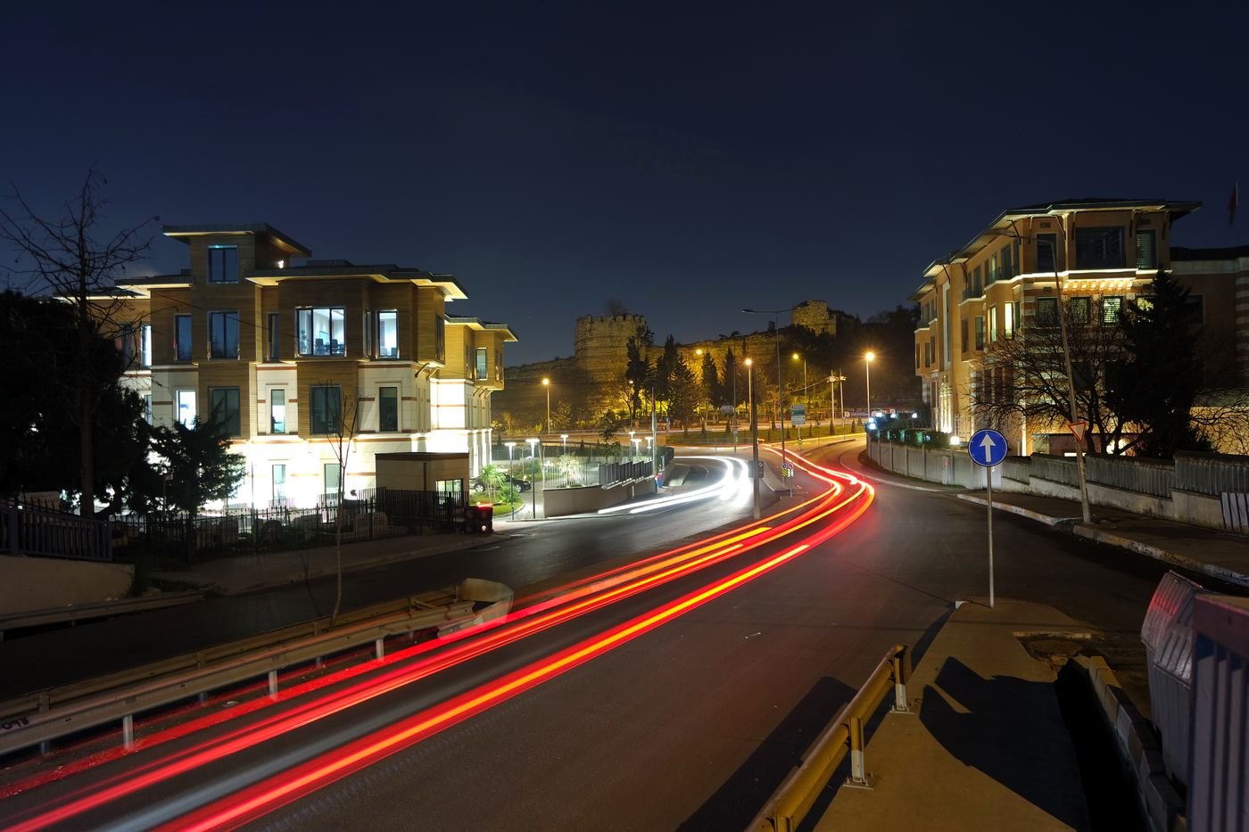 A wide night street lit by streaking vehicle lights
