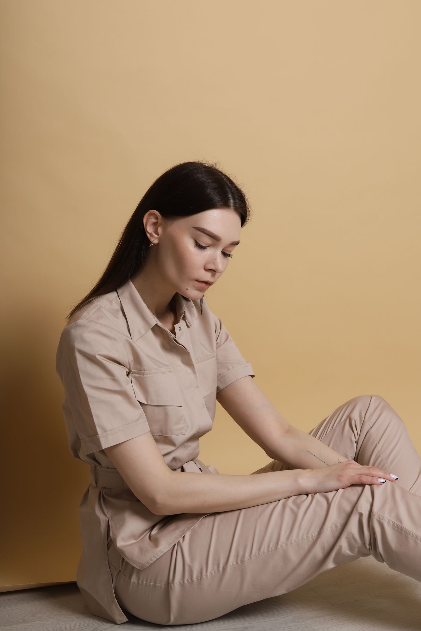 A portrait in warm neutral tones against a sand-coloured backdrop