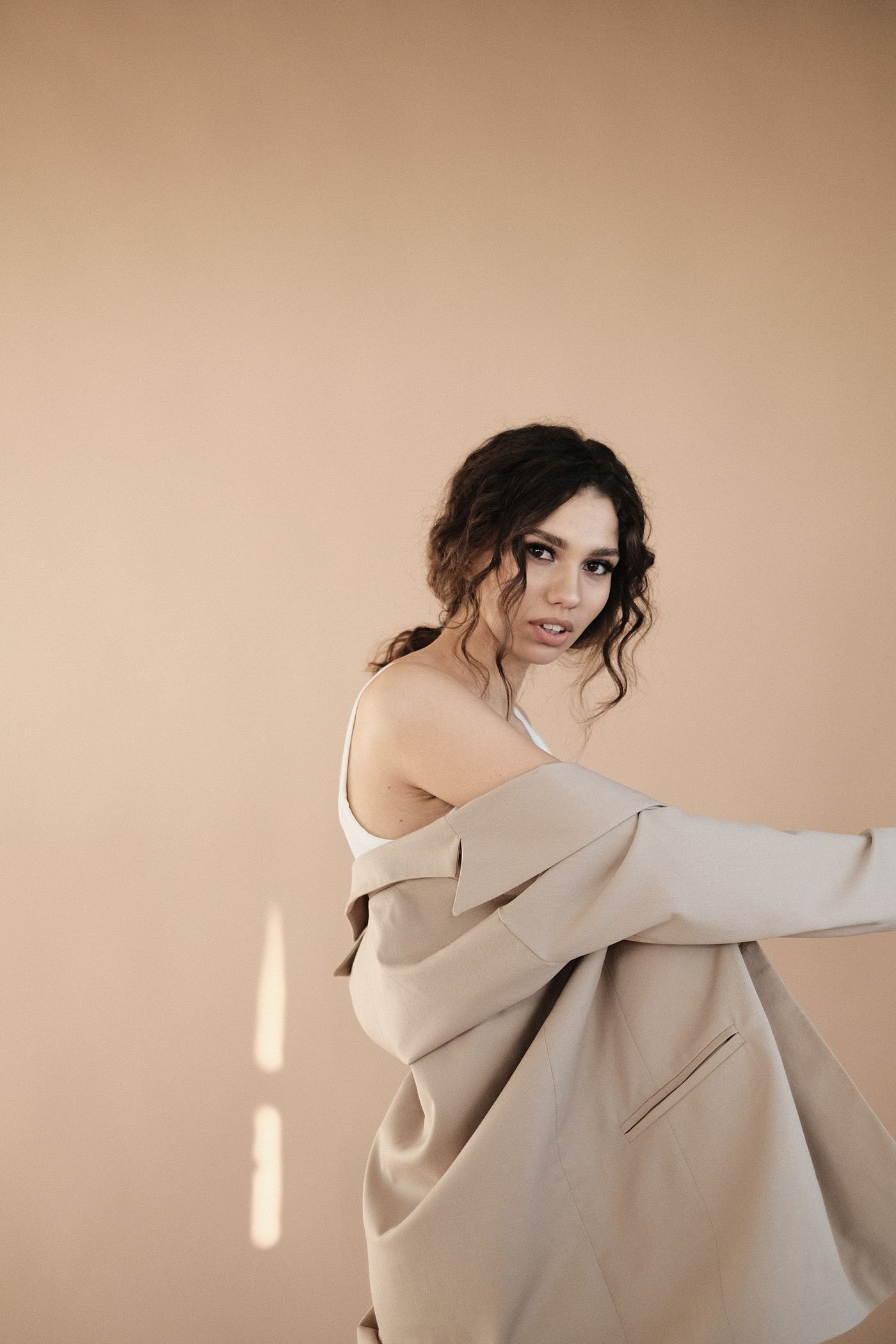 A figure in a soft cream coat against a warm backdrop